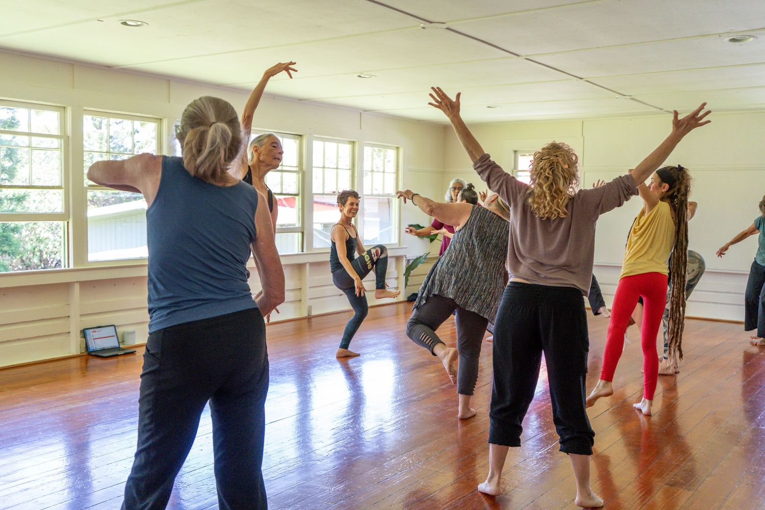 A group of people participating in a dance fitness class with raised arms in a bright studio space.