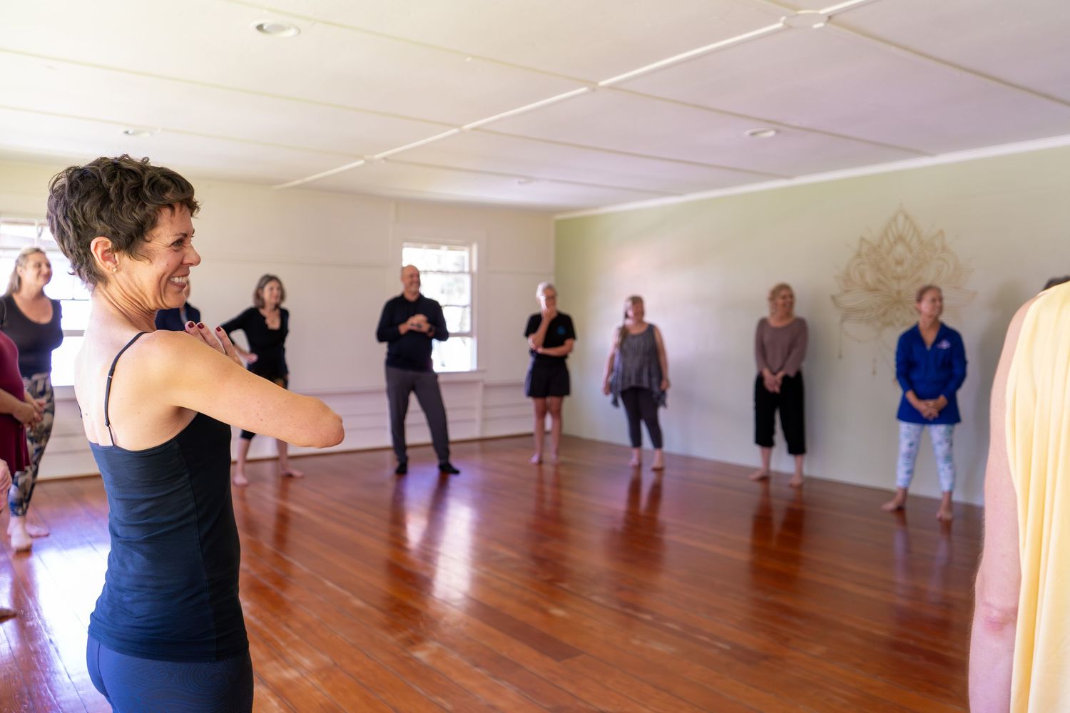 A group of people participating in a dance or exercise class in a bright studio space with wooden floors.