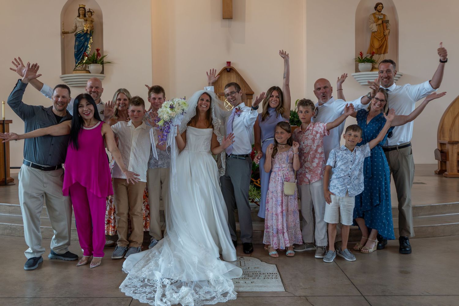 Wedding party celebrating in a church with bride in white gown and guests cheering with raised arms.