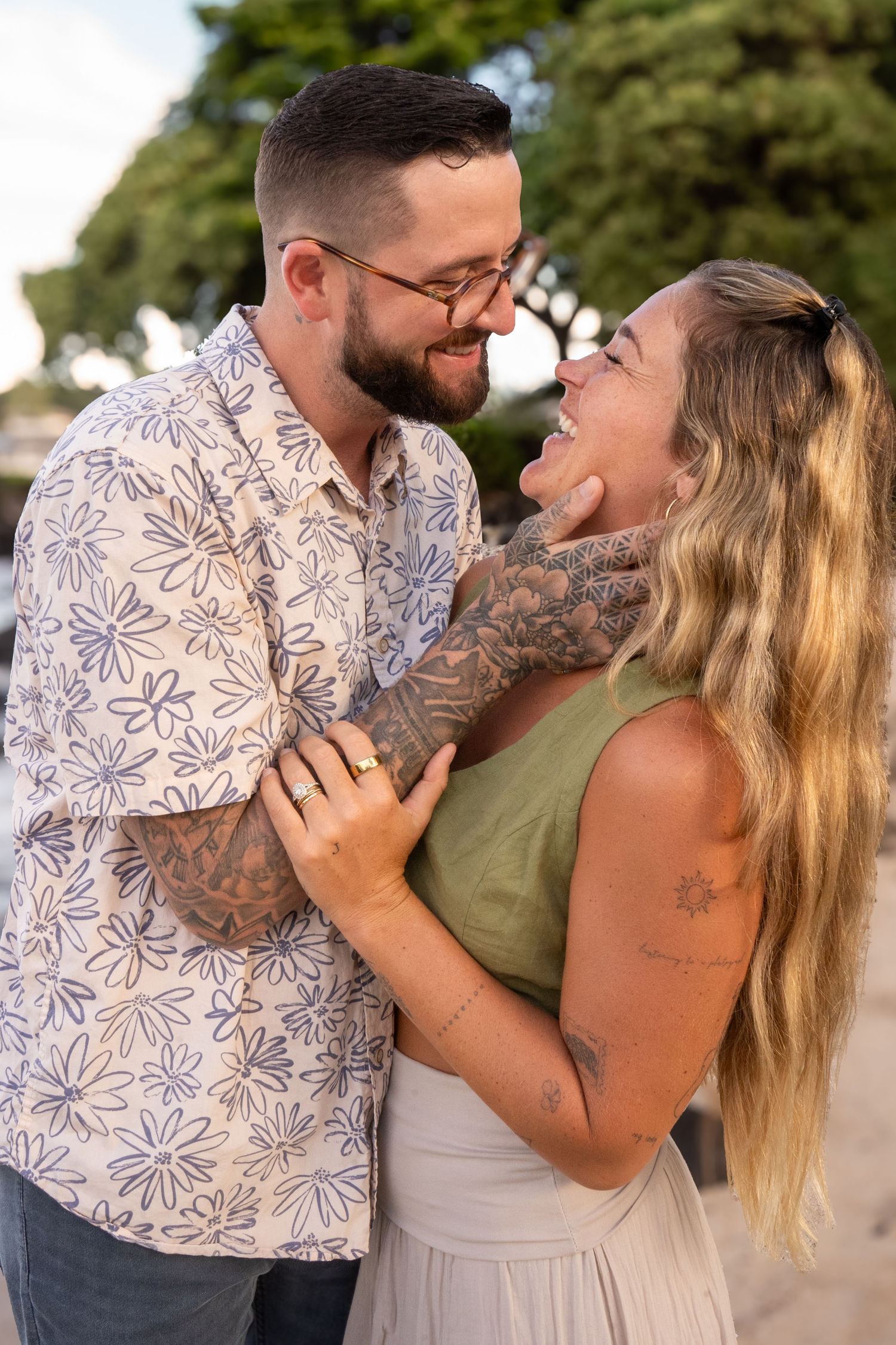 A couple laughs and embraces while sharing a romantic moment outdoors during a sunny day.