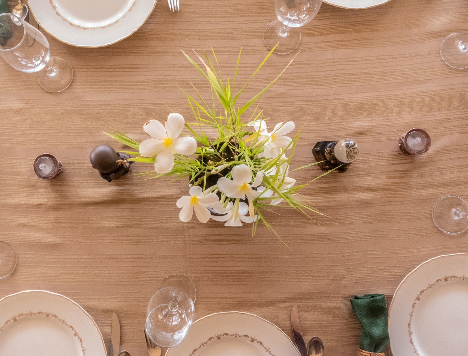 Overhead view of elegant table setting with white plates and wine glasses on wooden surface.