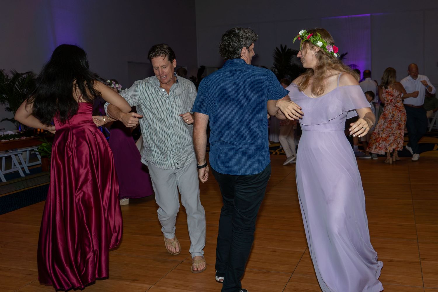 Guests dancing joyfully at a wedding reception, including a woman in a lavender gown with a floral crown.