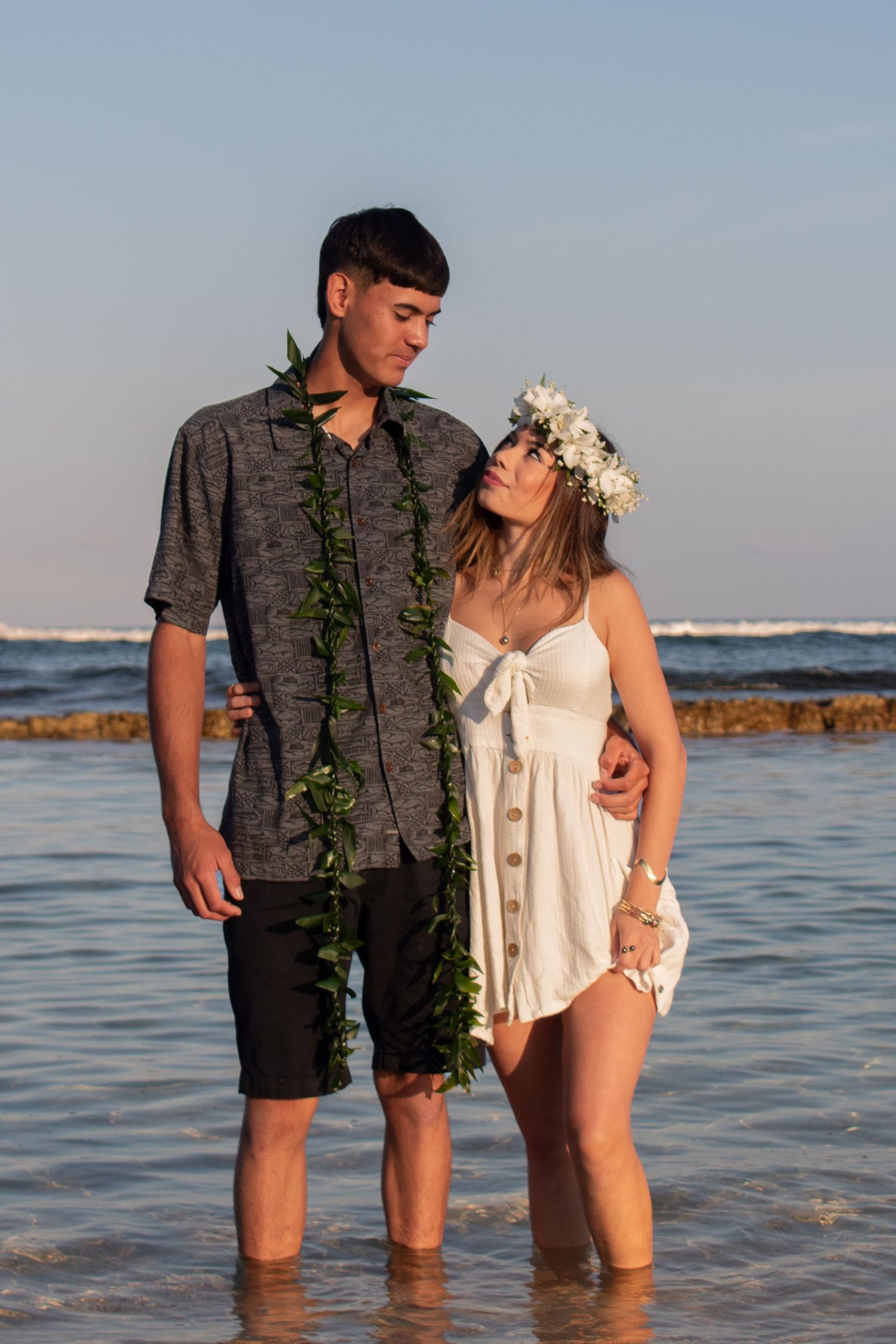 Couple standing in ocean water at sunset wearing casual beachwear.
