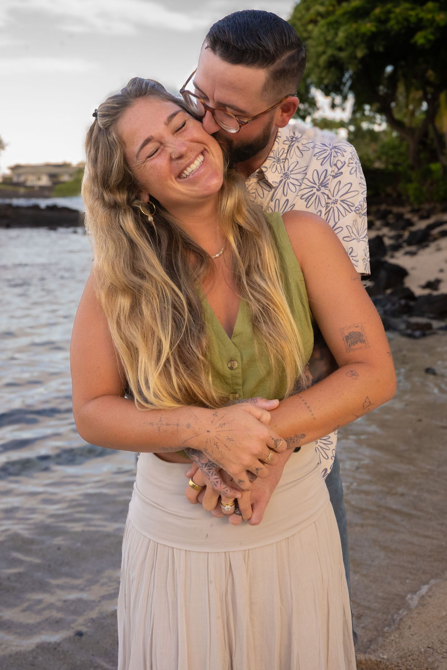 Romantic beach photoshoot of couple hugging and laughing by the ocean at sunset.