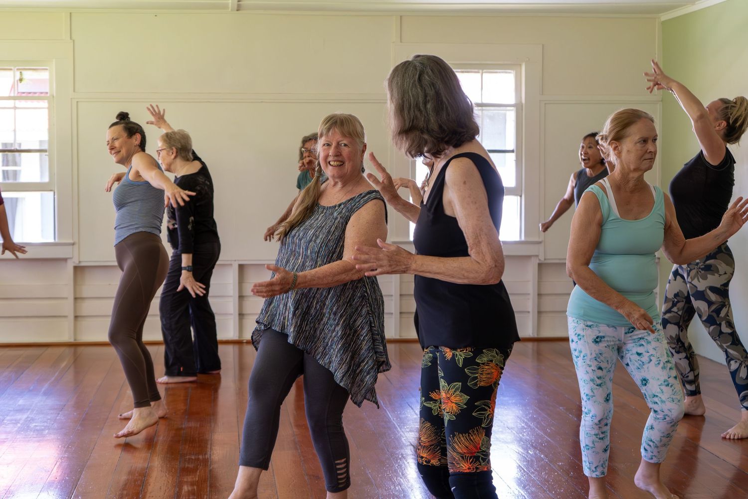 Group of dancers practicing together in a bright dance studio with wooden floors and white walls.