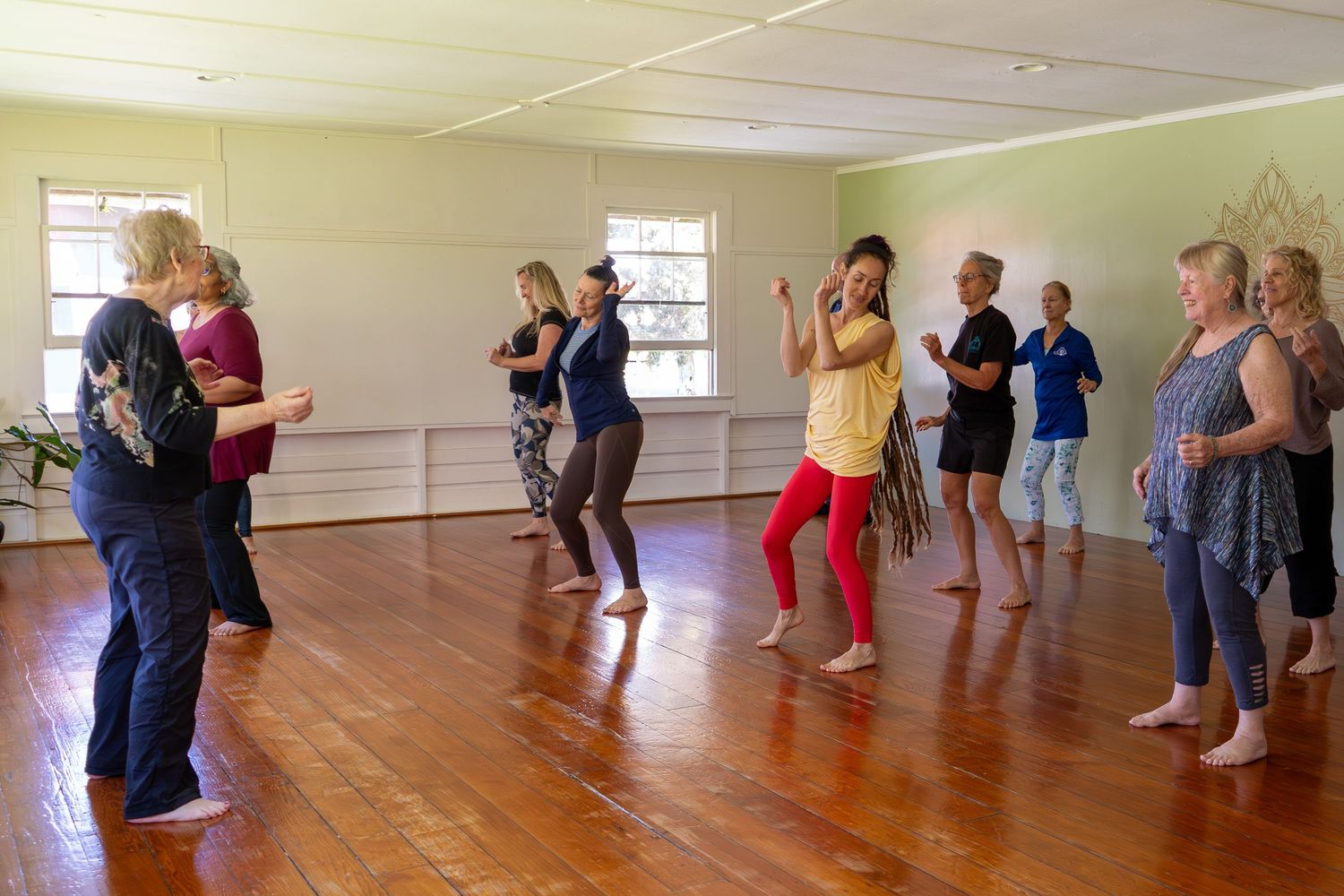 People practicing dance steps in a bright studio space with wooden floors and mirrored walls.