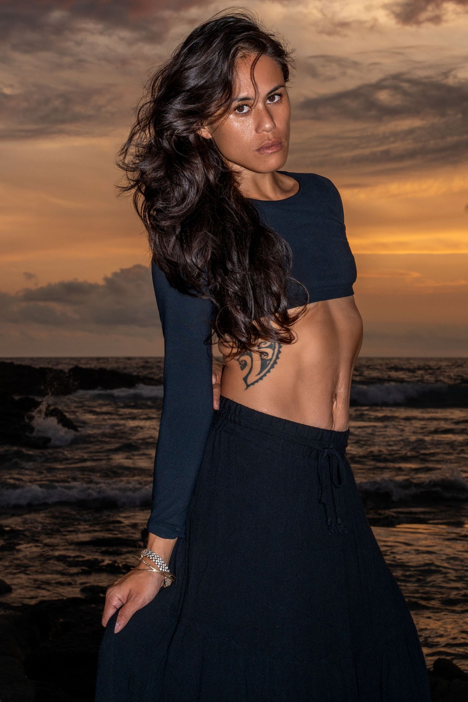 Silhouette poses against dramatic sunset sky over ocean waves.