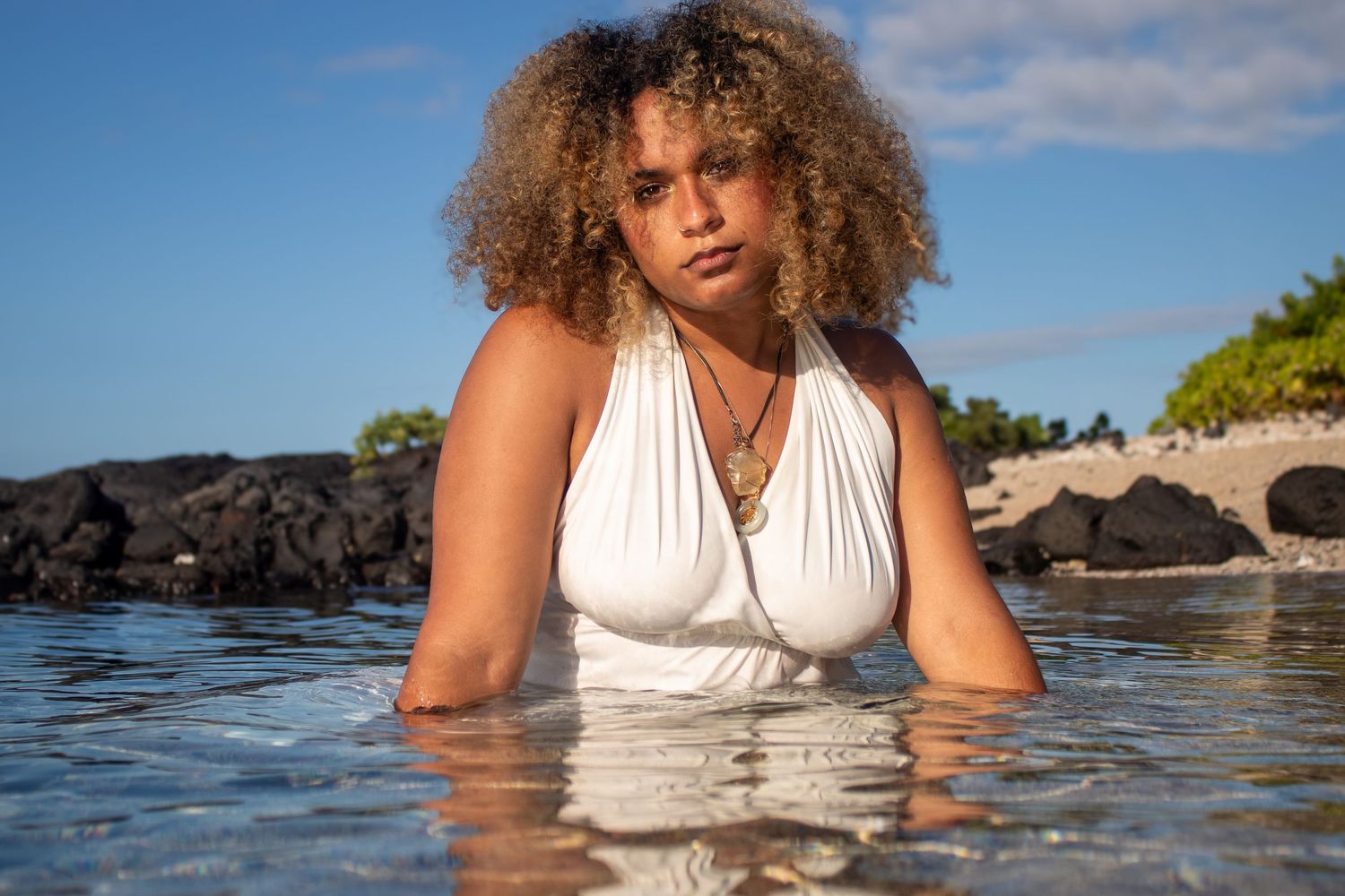 Woman with curly hair relaxing in ocean water wearing white swimwear.
