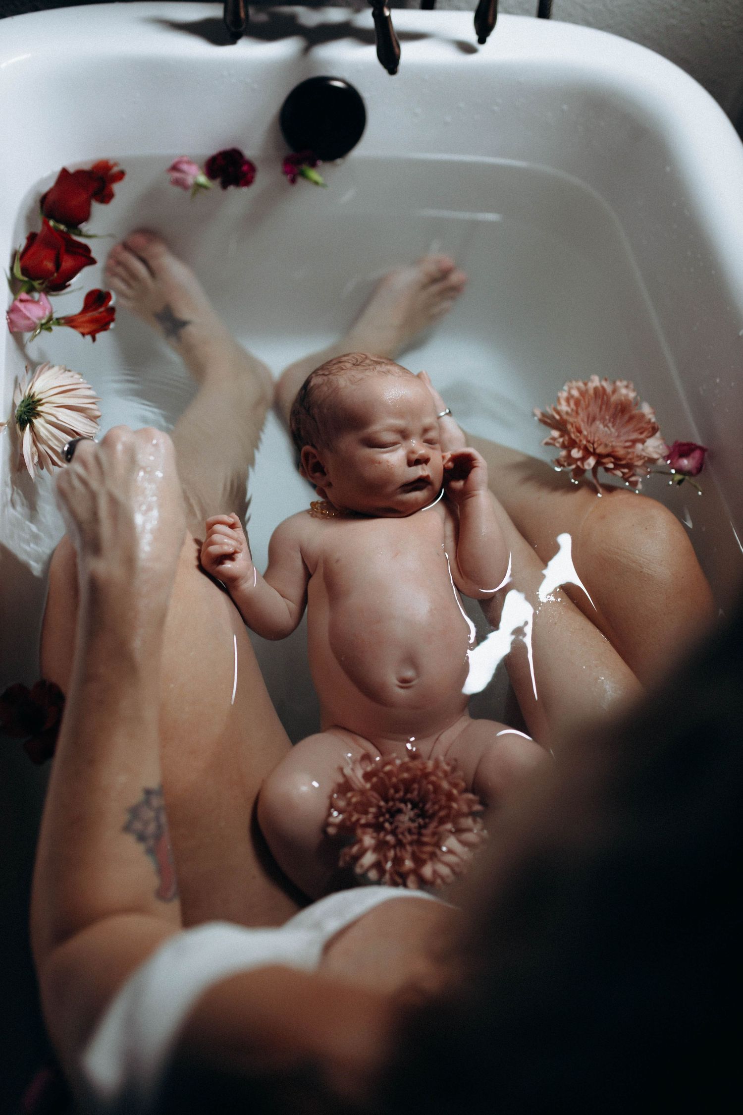 Baby playing in a bathtub with pink flowers and splashing water.