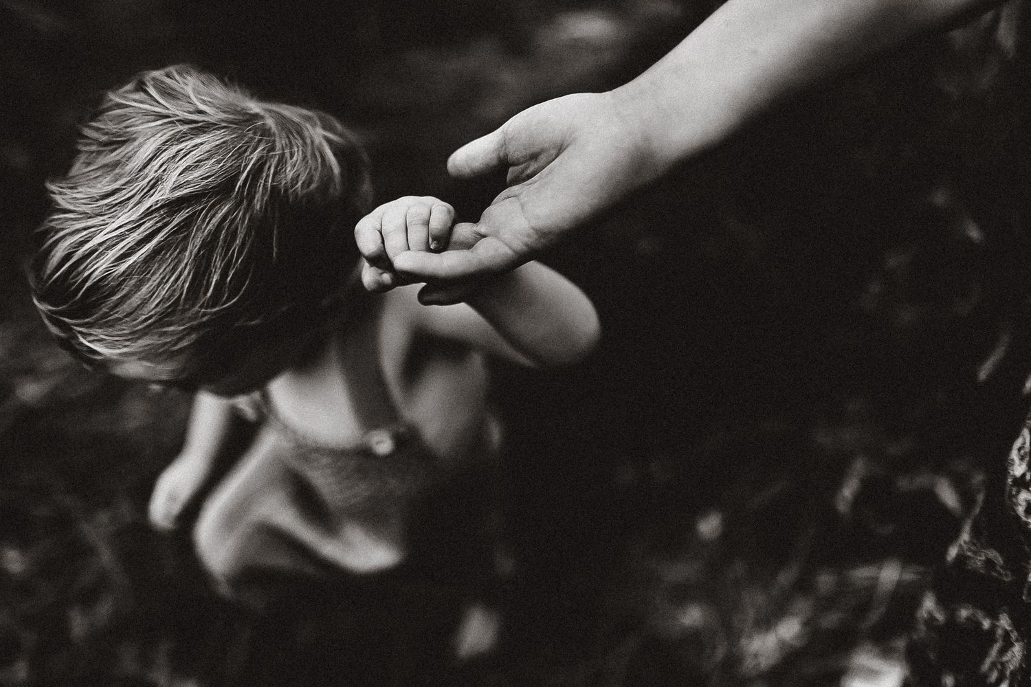 A black and white close-up photo shows a hand gently touching a person's hair in soft lighting.
