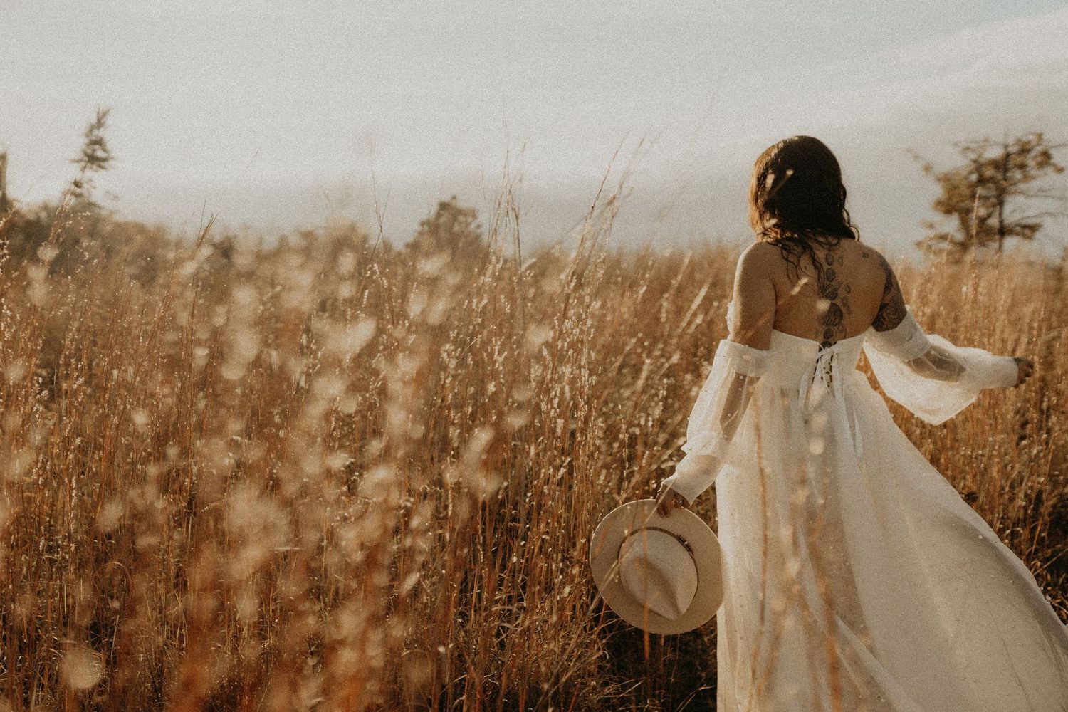 A romantic sepia-toned wedding scene with flowing white dress silhouetted against a golden field at sunset.