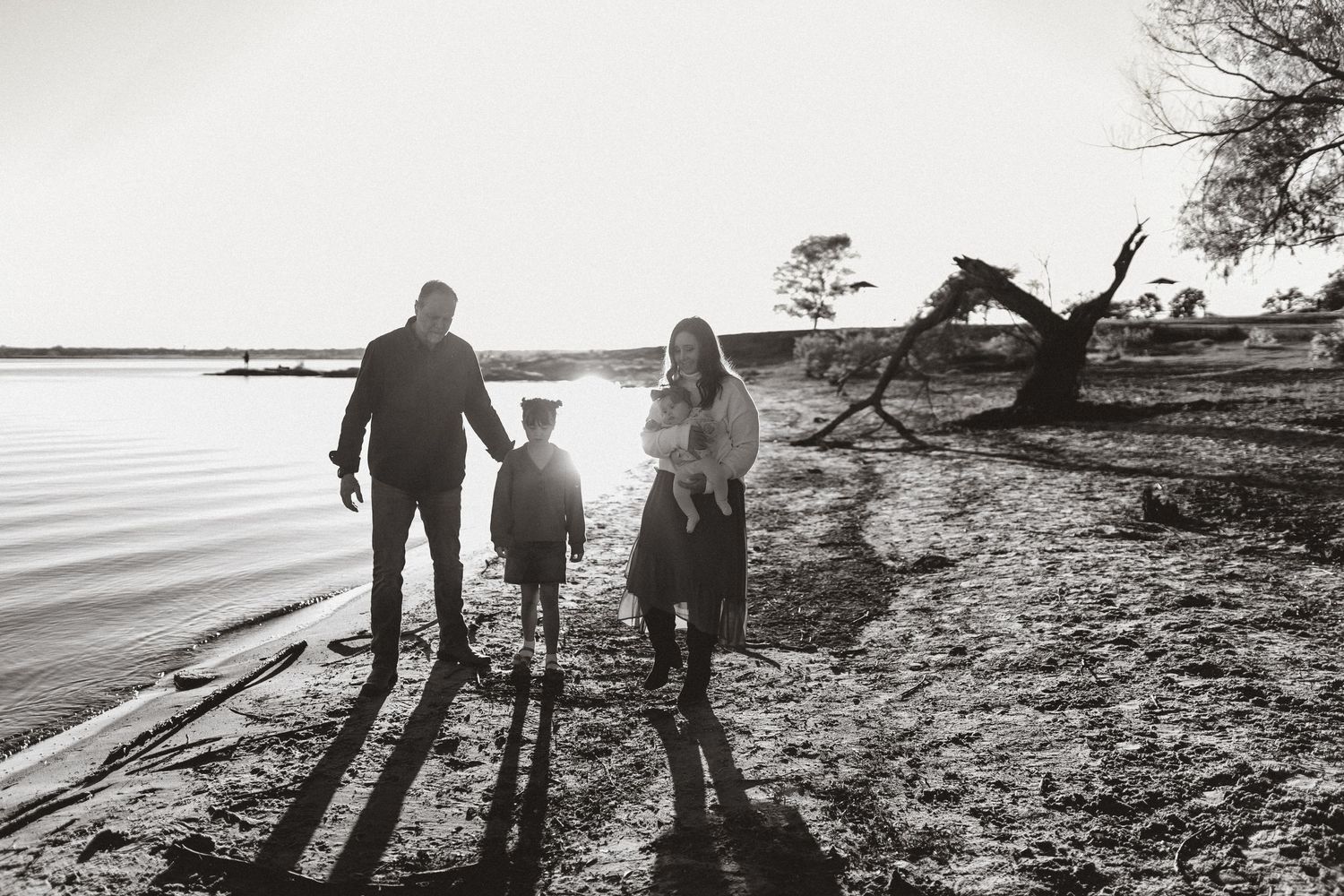 Silhouettes of a family walking along a beach shoreline at sunset casting long shadows on the sand.