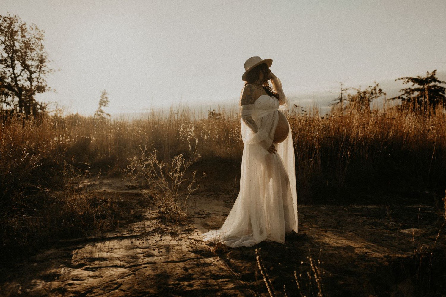 A romantic couple in wedding attire embraces in a golden field at sunset creating a dreamy silhouette.