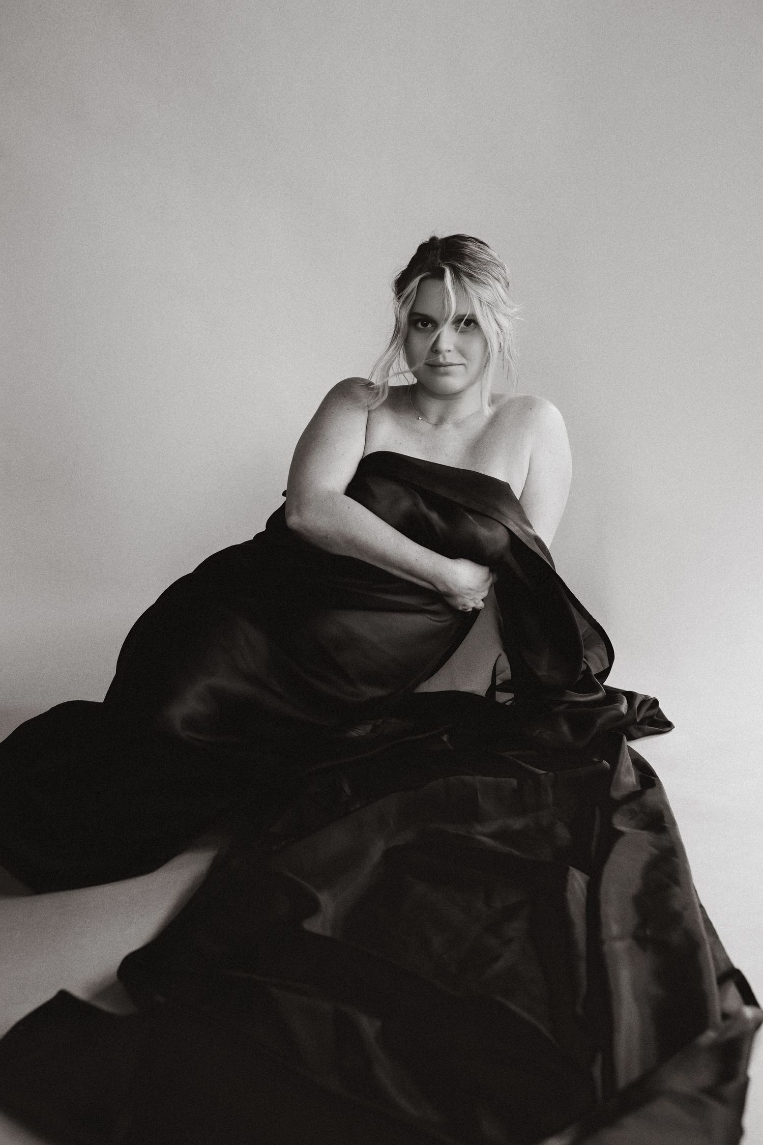 A series of black and white artistic photographs showing a figure draped in dark fabric against a light background.