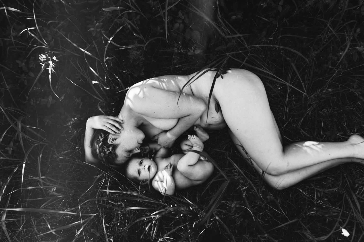 Black and white fine art maternity and motherhood portrait of a mother lying in grass holding her baby