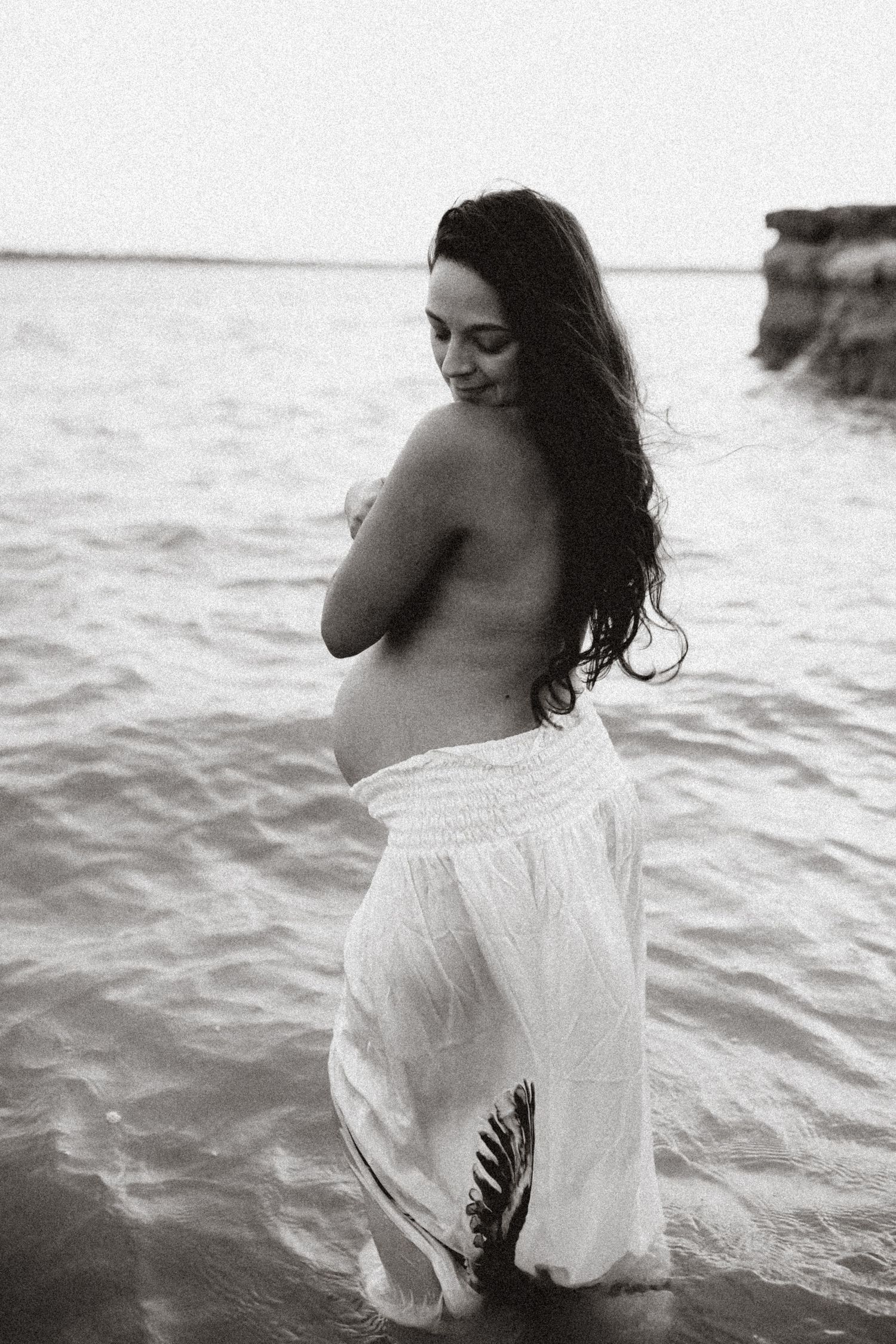 Artistic black and white photos of figure in white dress wading into ocean water.