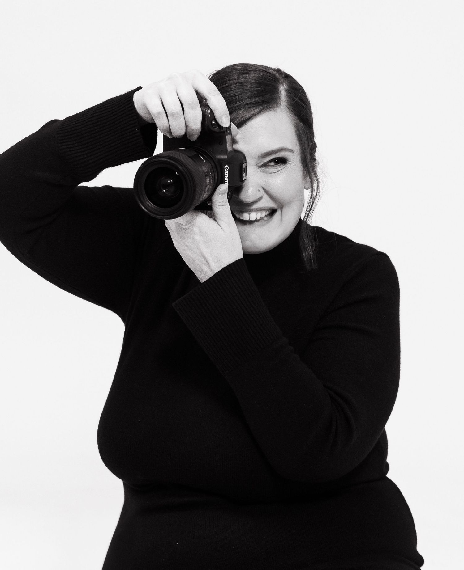 Black and white portrait of Sarah Maverick, Dallas maternity photographer, holding her camera in studio.