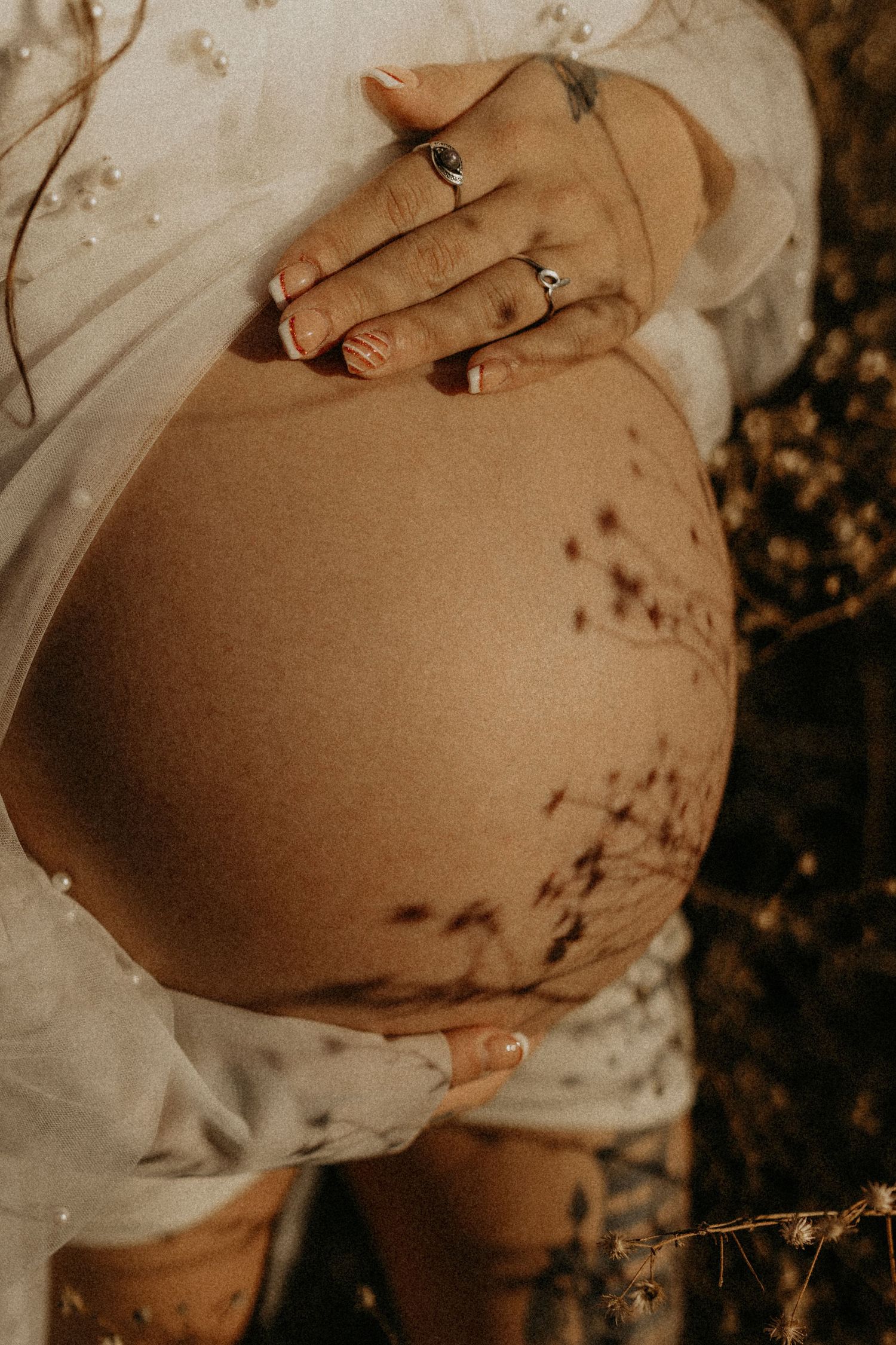 A close-up series of a pregnant belly being gently touched by hands wearing rings in warm, sepia-toned lighting.