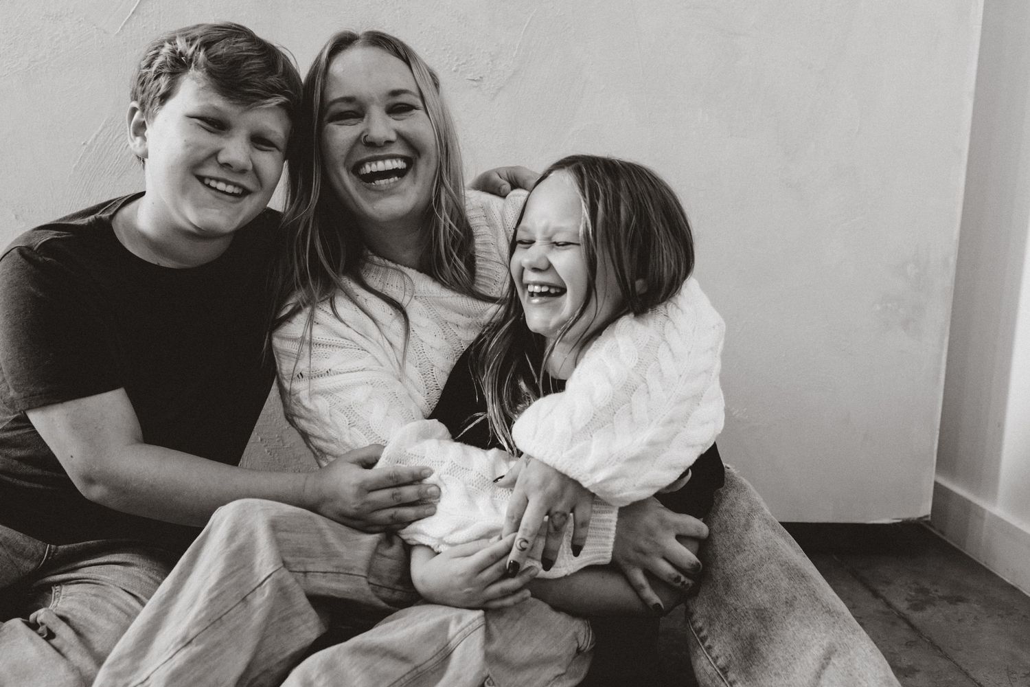 A group of people laughing and embracing while sitting together in a casual indoor setting.