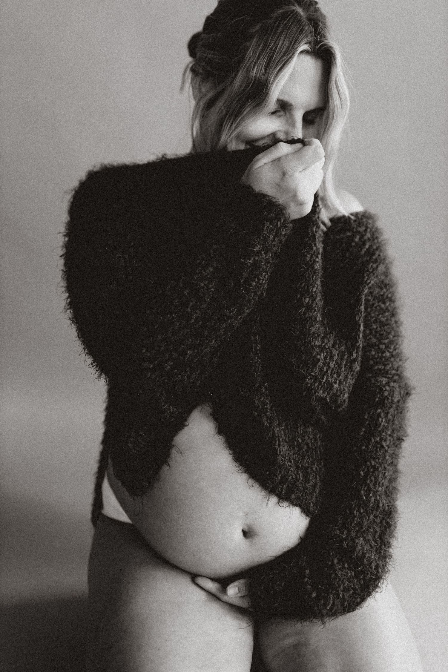 Black and white artistic portrait showing figure in fuzzy sweater with exposed midriff against plain background.