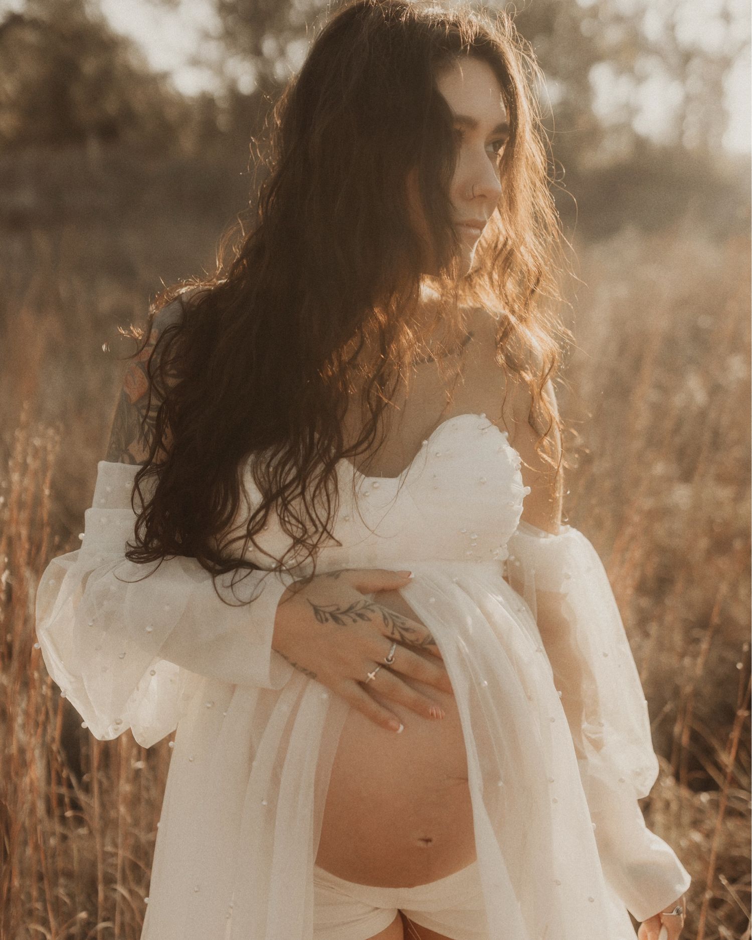 A figure in a flowing white dress stands in a golden sunlit field during sunset, creating a dreamy ethereal atmosphere.