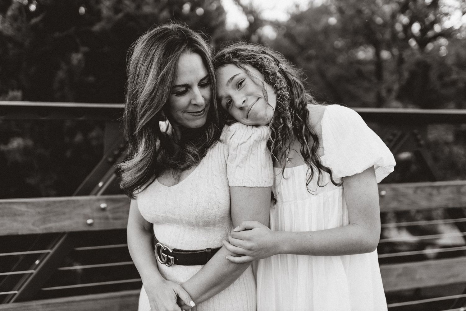 Two people in white outfits embrace and laugh together while sitting outdoors in black and white photography.