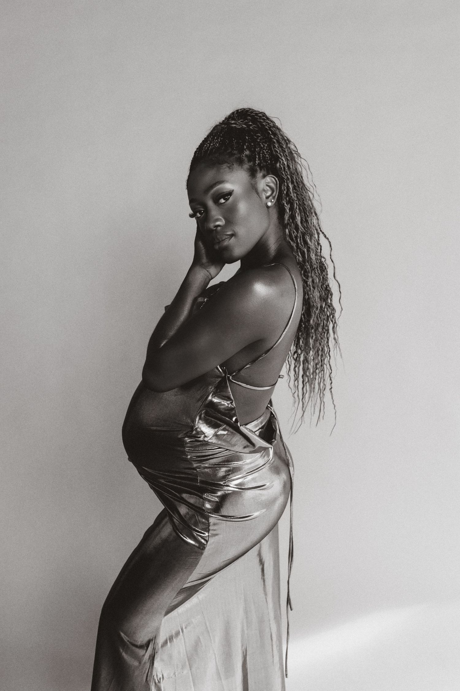 Black and white portrait of a woman in a silky dress posing elegantly against a plain background.