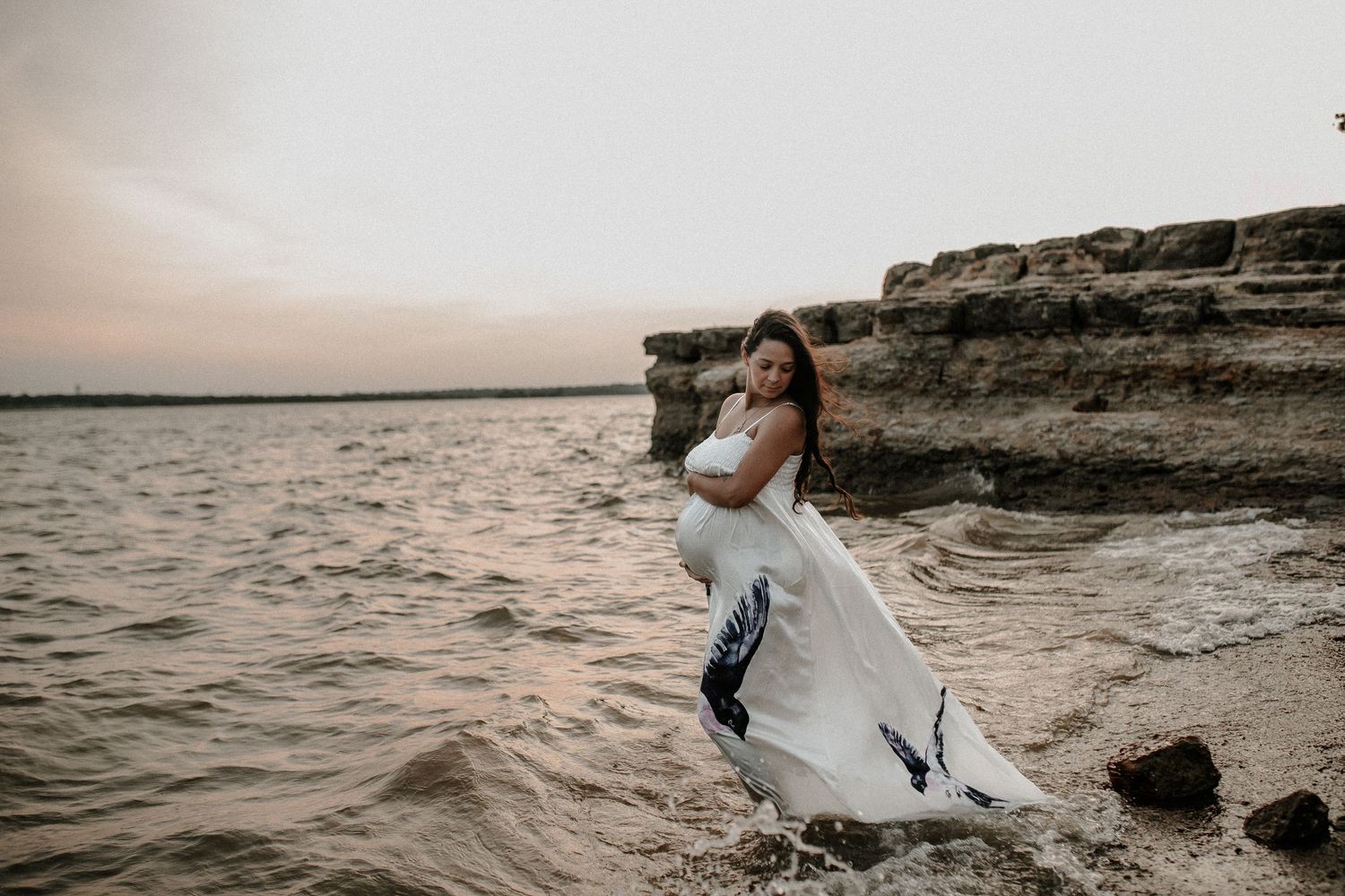 Dramatic seaside maternity portrait of a pregnant woman standing in the water near rocky coastal cliffs