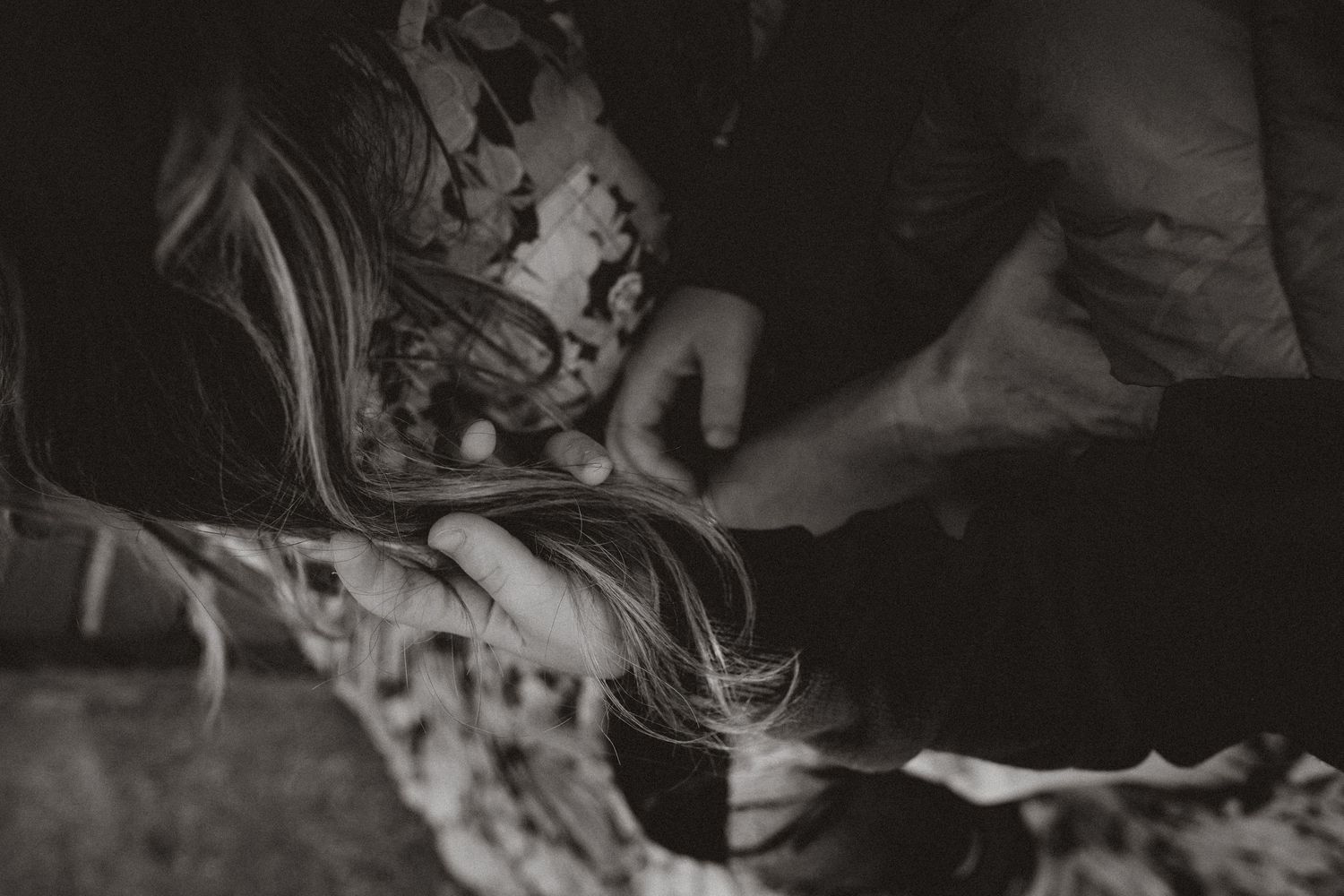 Black and white intimate photograph showing gentle hands comforting someone lying down in a dark setting.