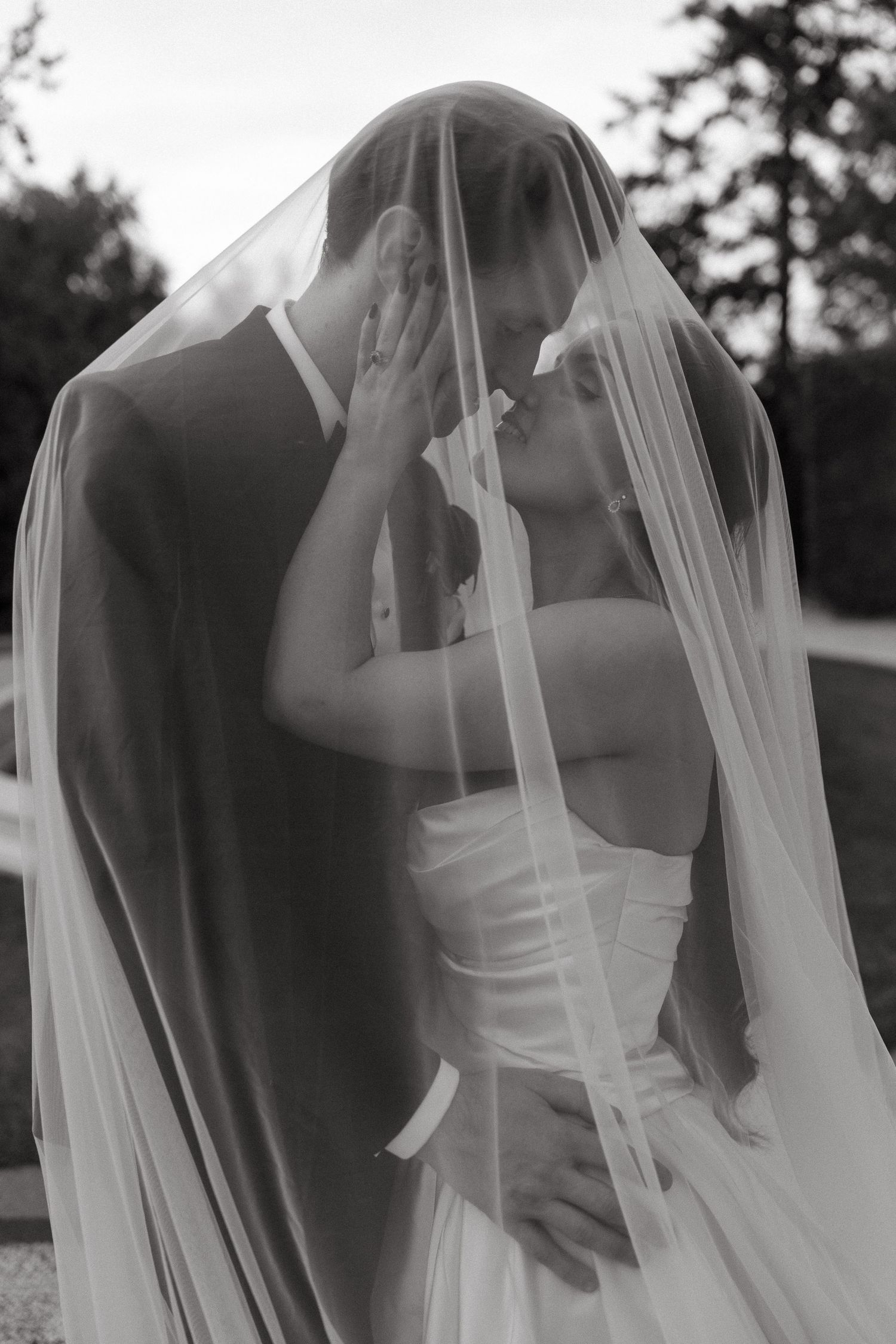 Black and white photo of bride and groom sharing a romantic moment under a flowing wedding veil.