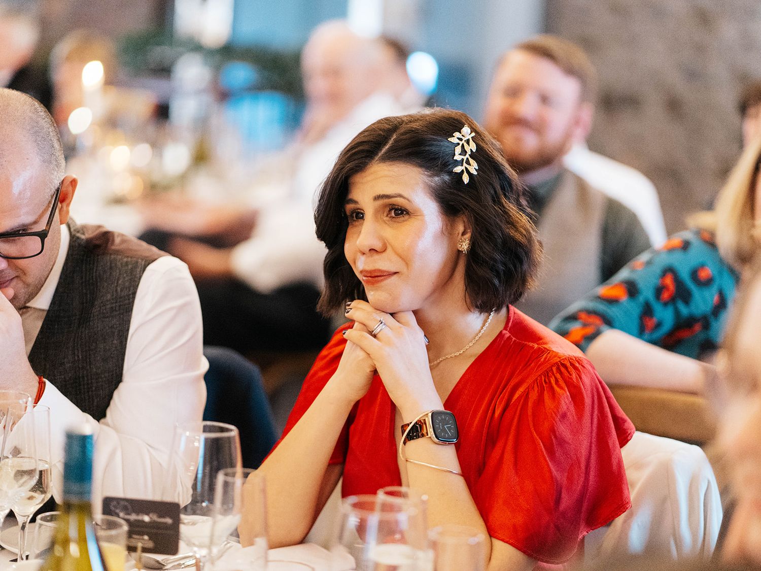 Wedding guest in a vibrant red dress rests her chin on her hand while seated at a reception dinner table.