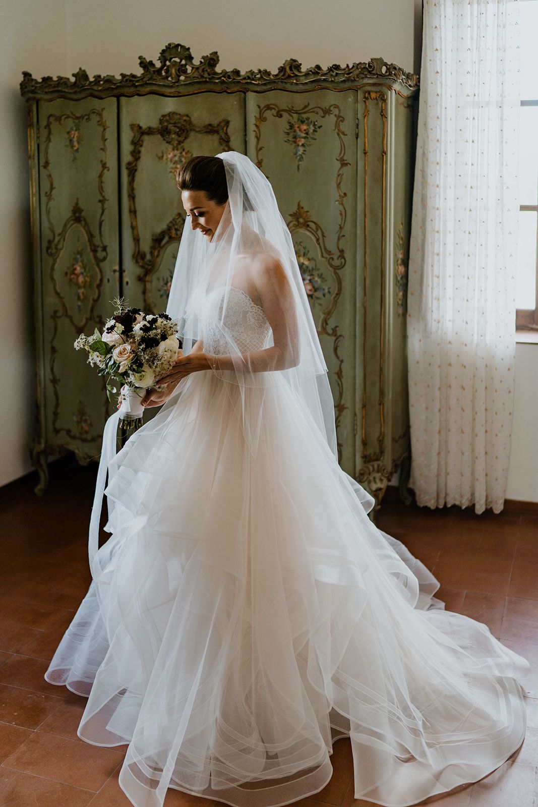 A flowing white wedding gown with a dramatic veil is showcased in an elegant room with ornate wall panels.