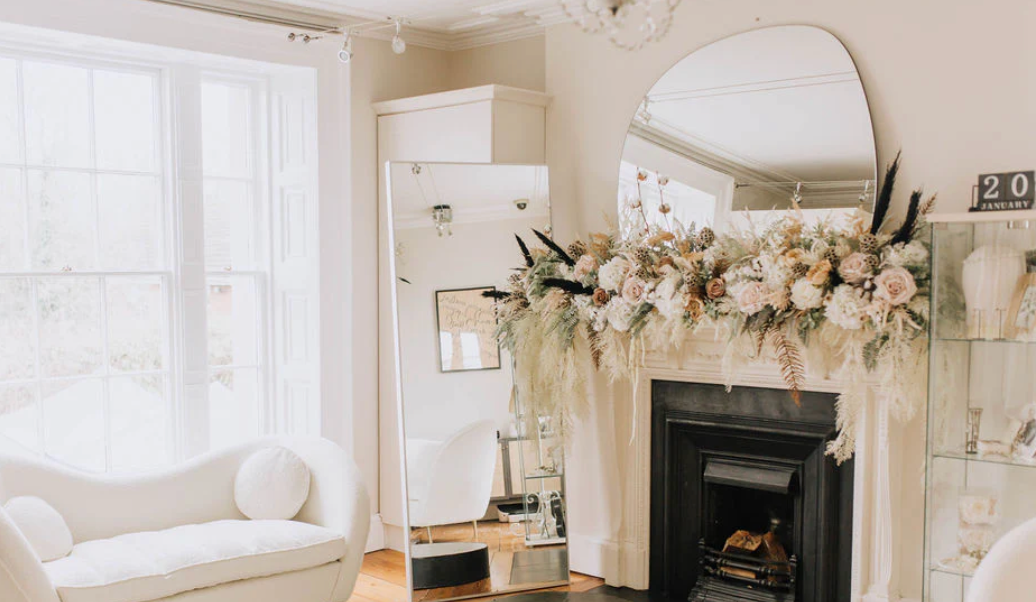 A bright and airy white farmhouse living room features rustic decor, floral garlands, and cozy seating arrangements.