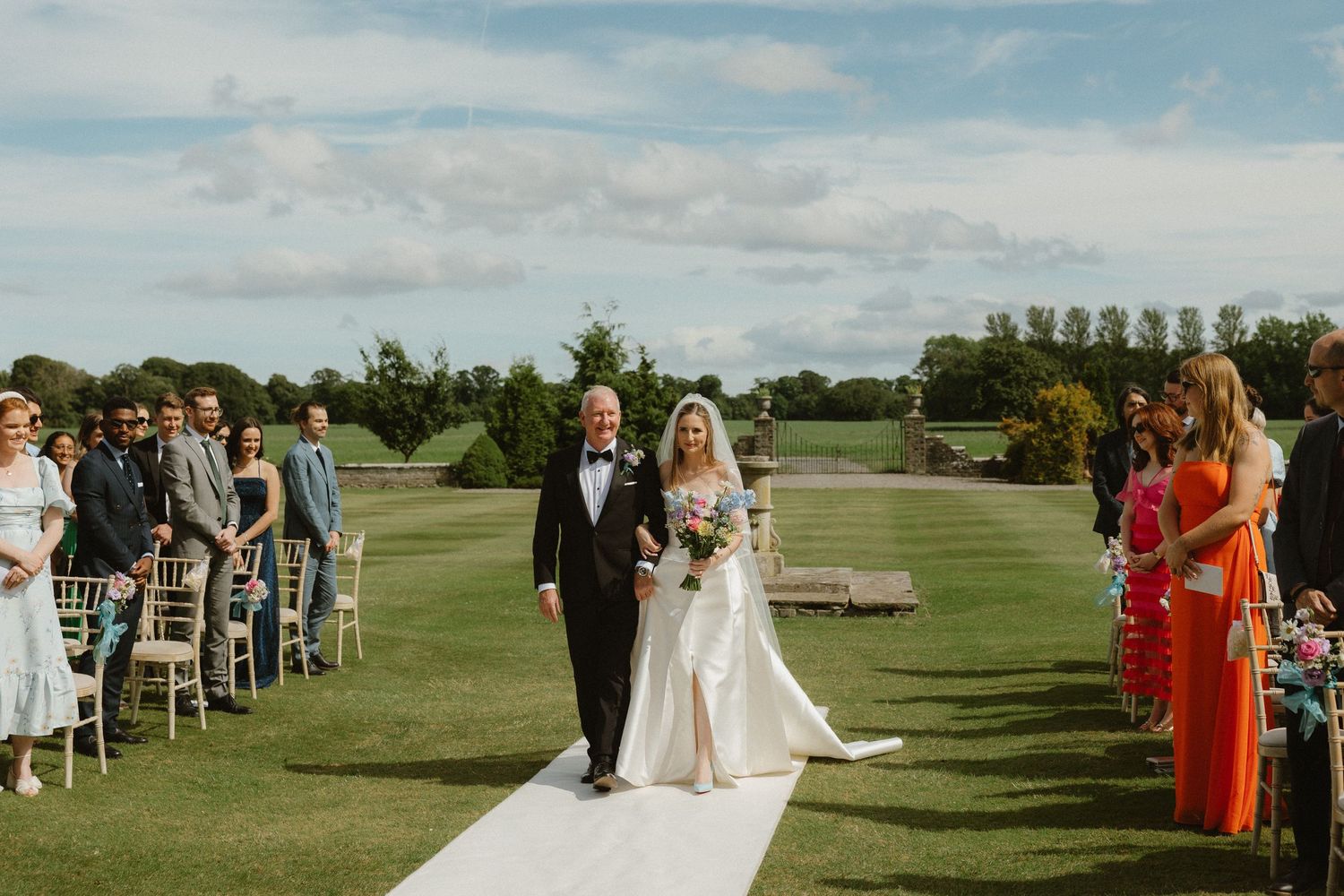 Outdoor wedding ceremony setup on a lush green golf course with white chairs and decorative elements under blue skies.
