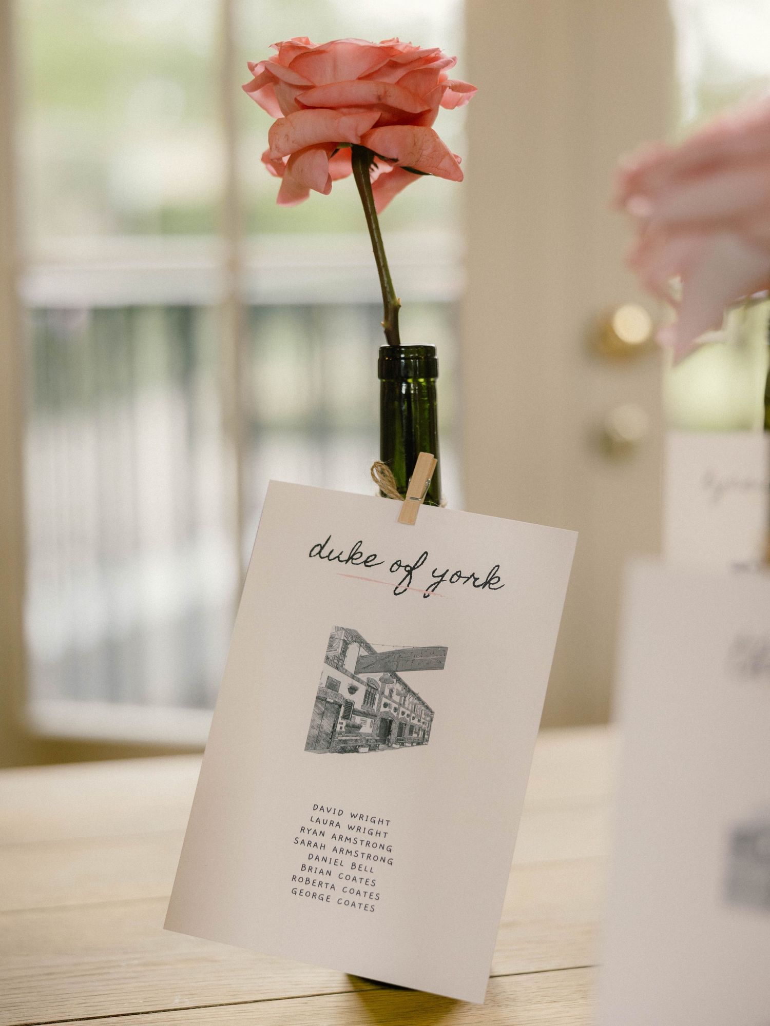 Elegant place cards with architectural sketches displayed in small vases with pink roses.