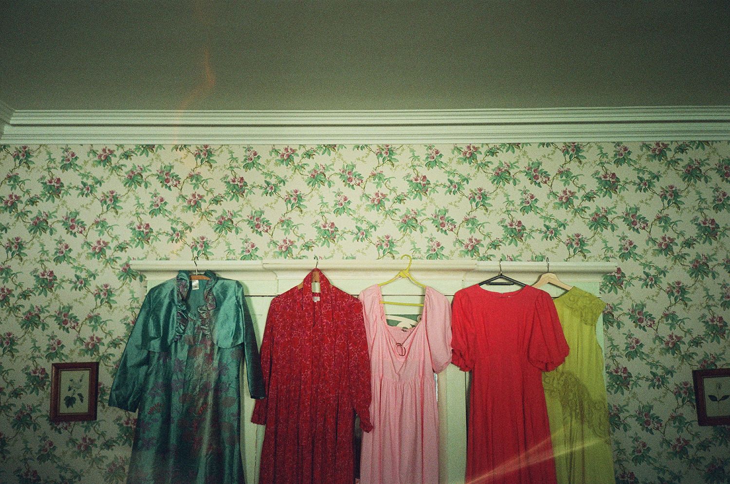 Row of colorful dresses hanging on display against floral wallpaper in a room.