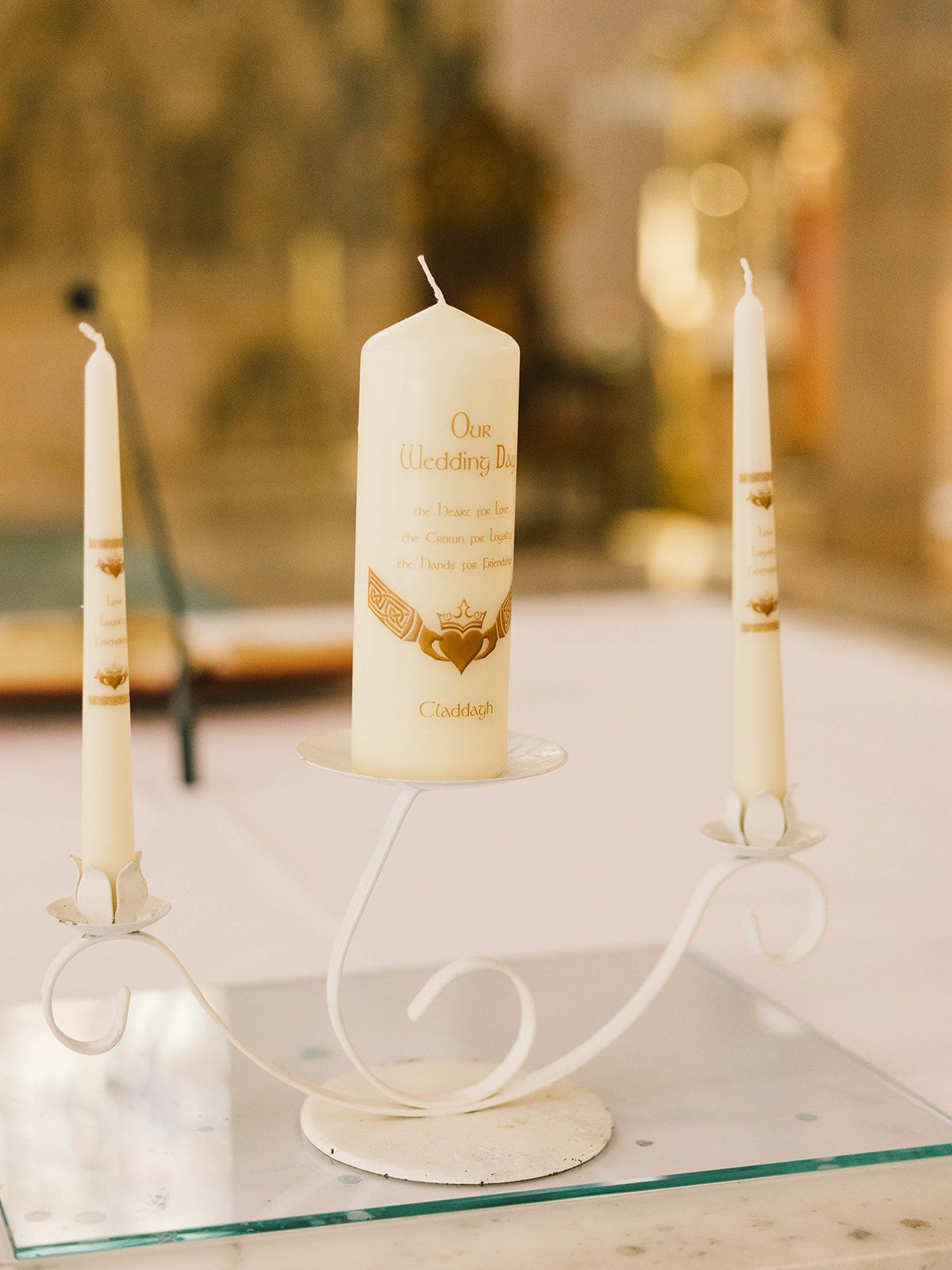 Three elegant white unity candles arranged on a glass surface with decorative metal holders for a wedding ceremony.