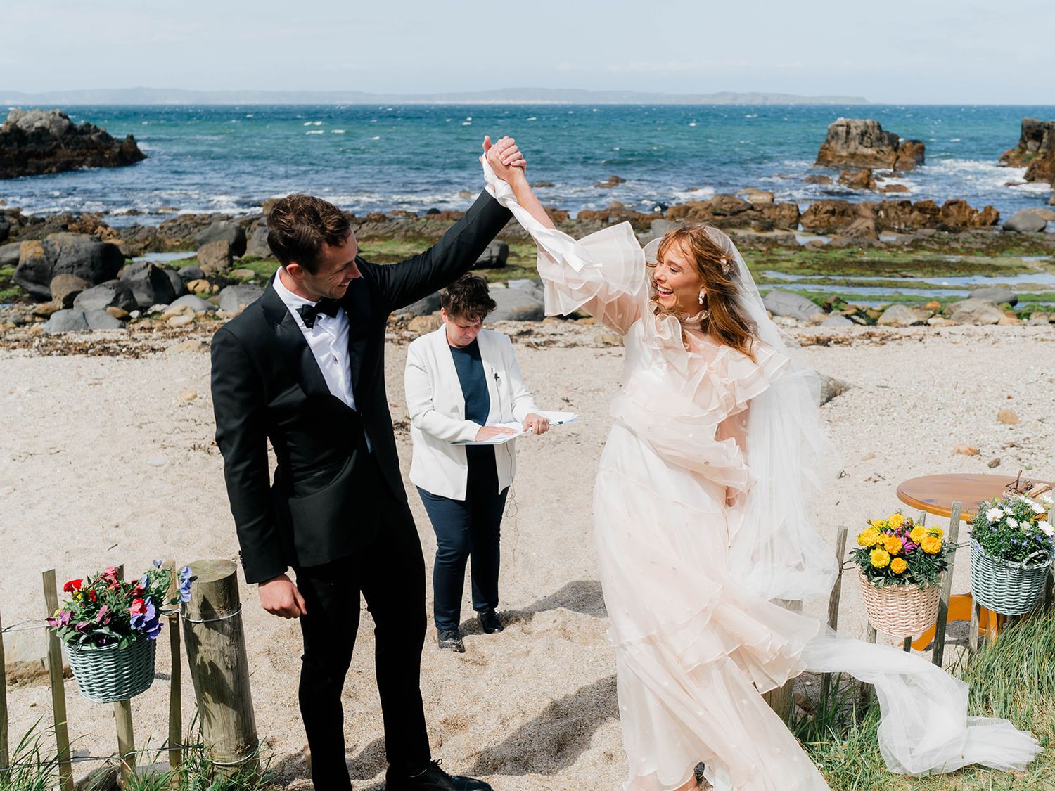 Newlyweds celebrate on beach with floral decorations and ocean backdrop.