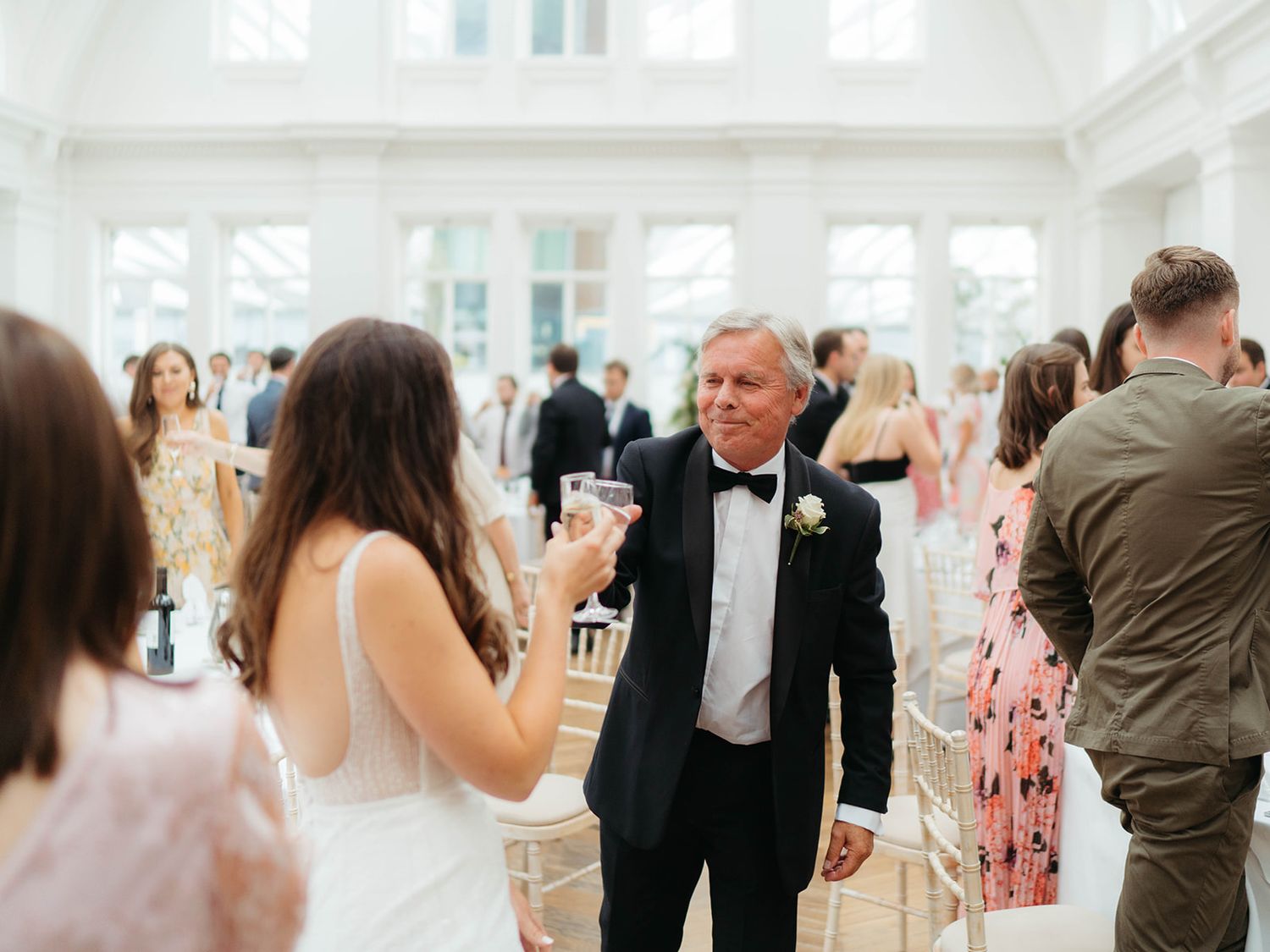 Wedding guests mingling in a bright, airy reception hall with tall windows and formal attire.