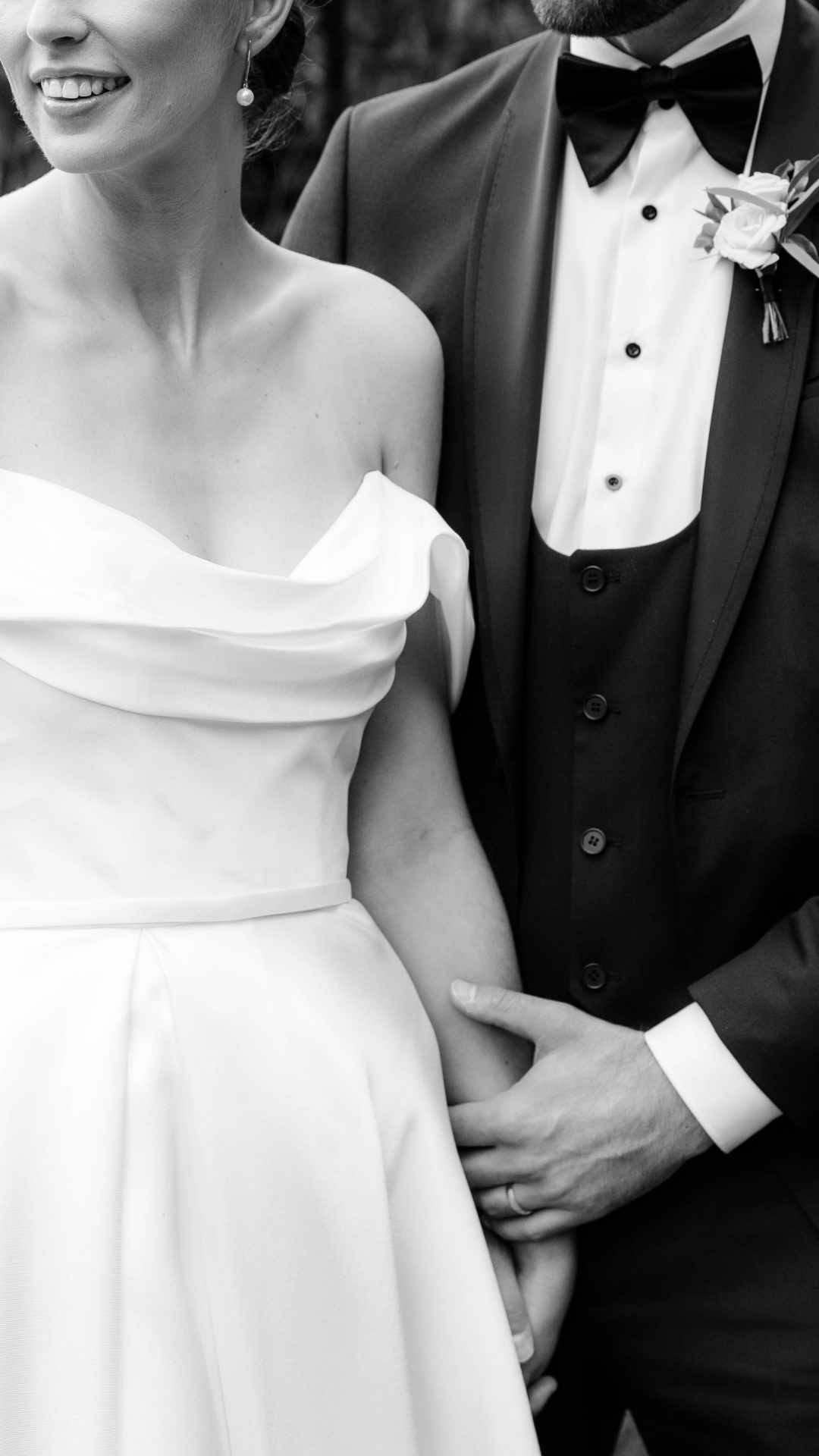 A black and white wedding photo showing details of a bride in an off-shoulder dress and groom in classic tuxedo with bow tie.