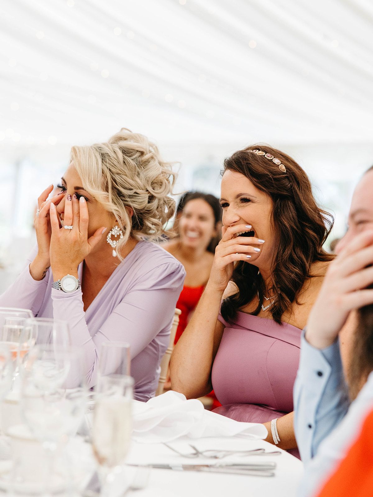 Guests laughing and covering their mouths while attending a reception at an elegant table setting.