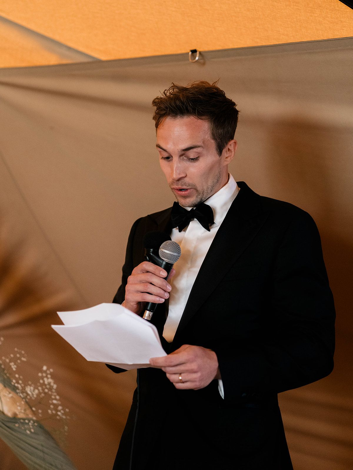 A speaker in black tie attire reads from paper during formal event speech.