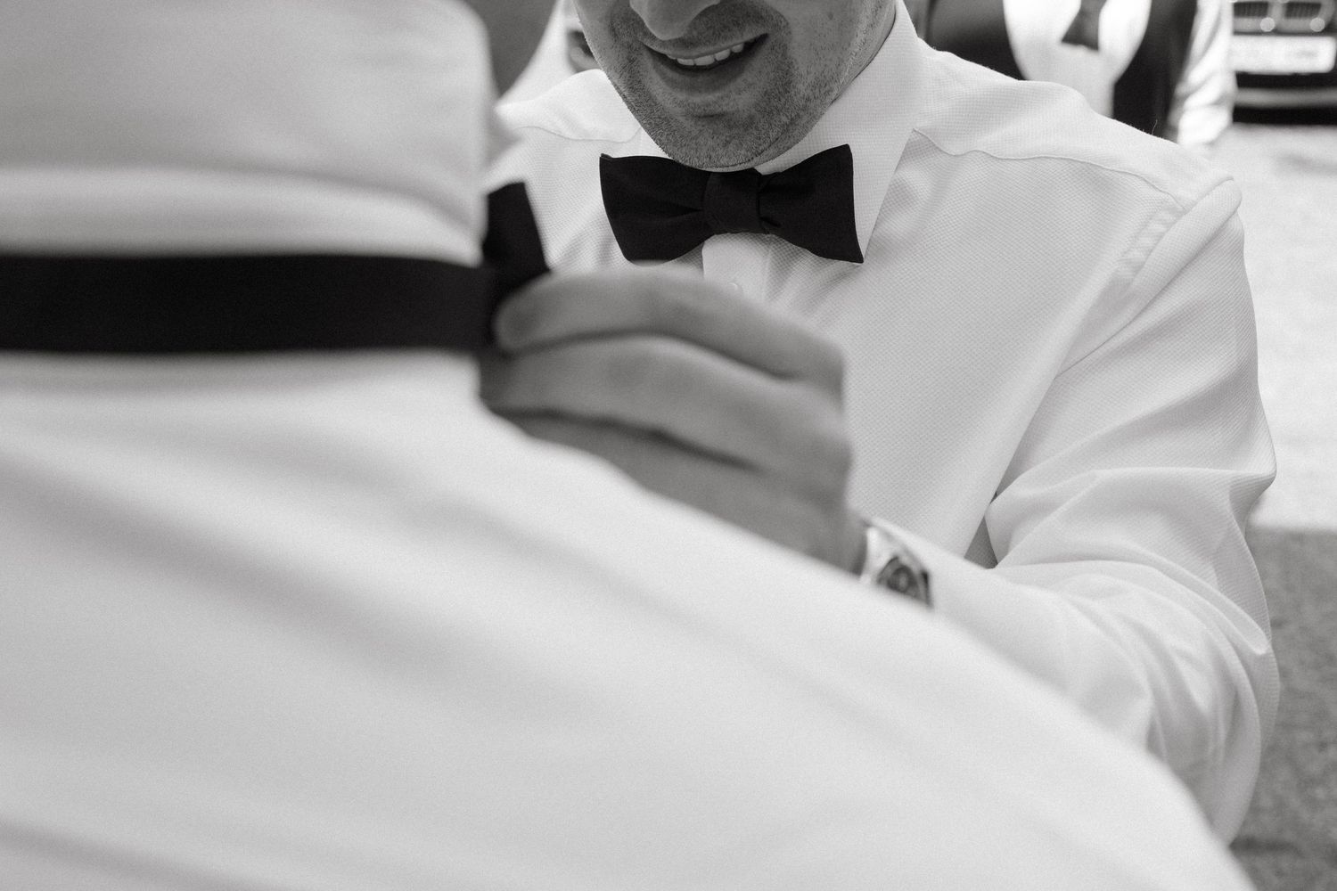 Close-up black and white shot of someone adjusting a bowtie at a formal event.
