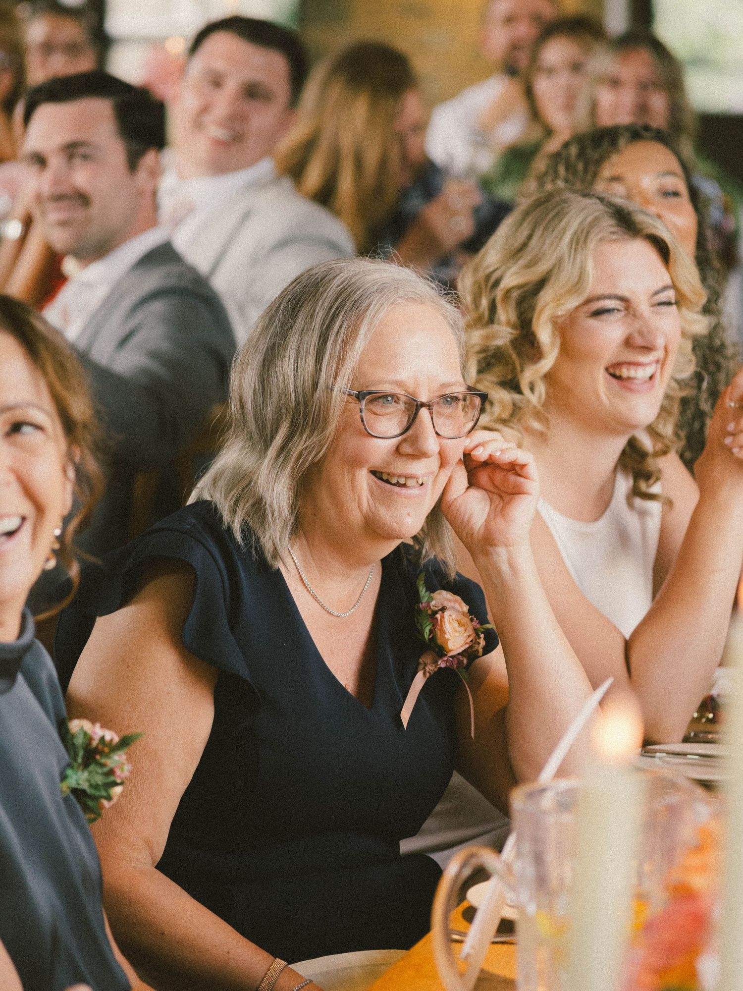 Wedding guests share joyful laughter during reception celebration at indoor venue.