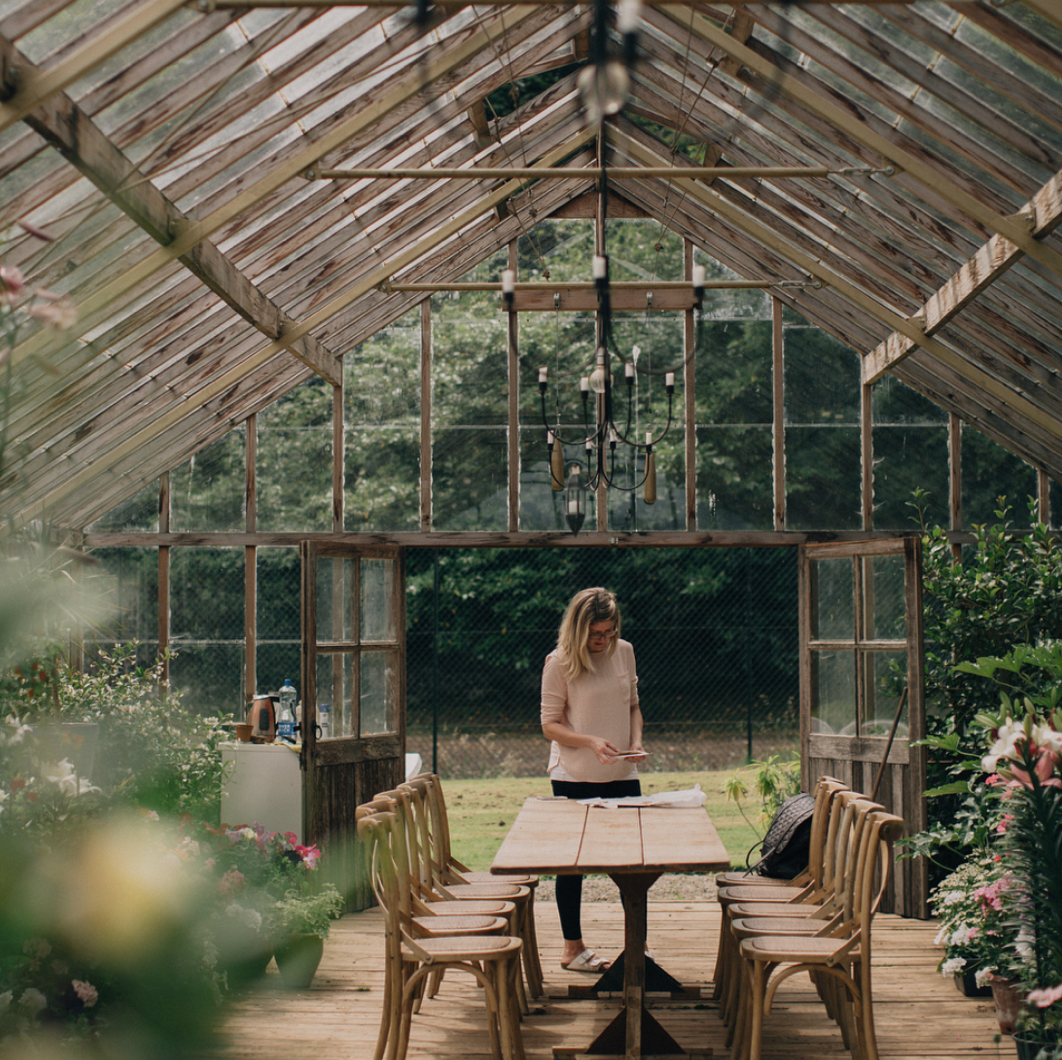 Rustic wooden greenhouse interior with natural light streaming through windows and wooden furniture setup for dining.