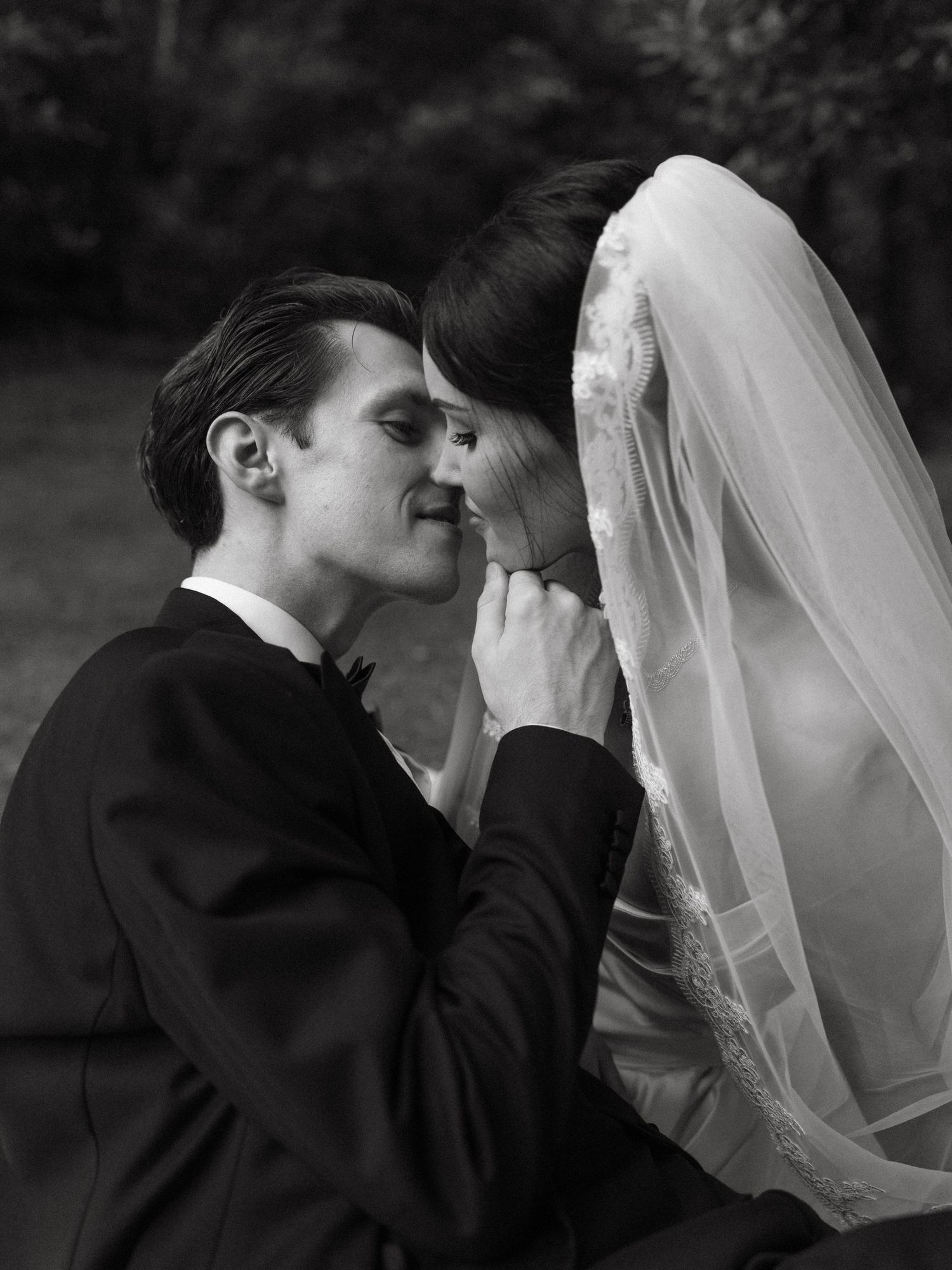 Black and white wedding photo of bride in veil and groom in suit sharing an intimate moment.