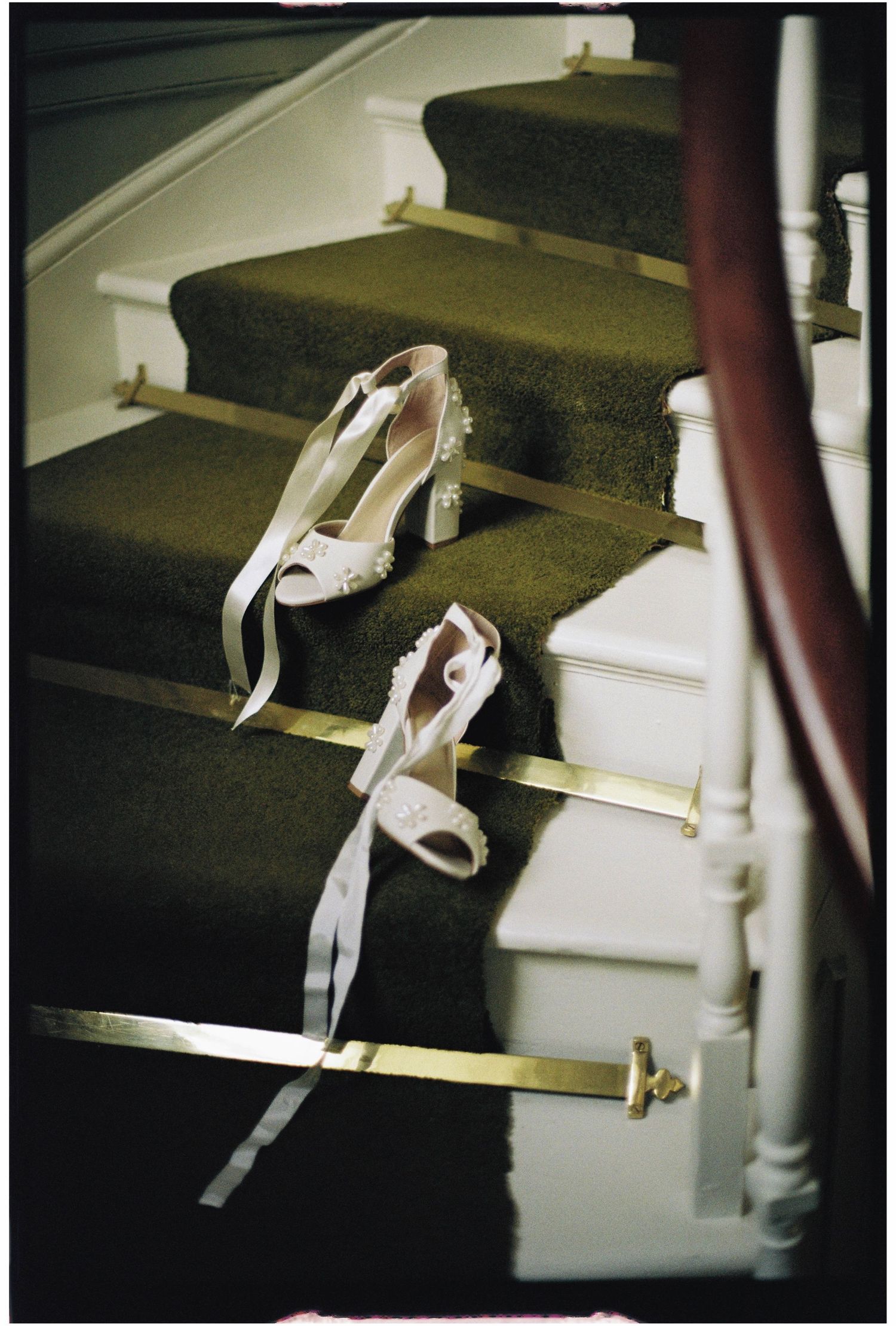 Elegant white lace bridal heels with ribbon ties rest on carpeted staircase steps at a wedding venue.