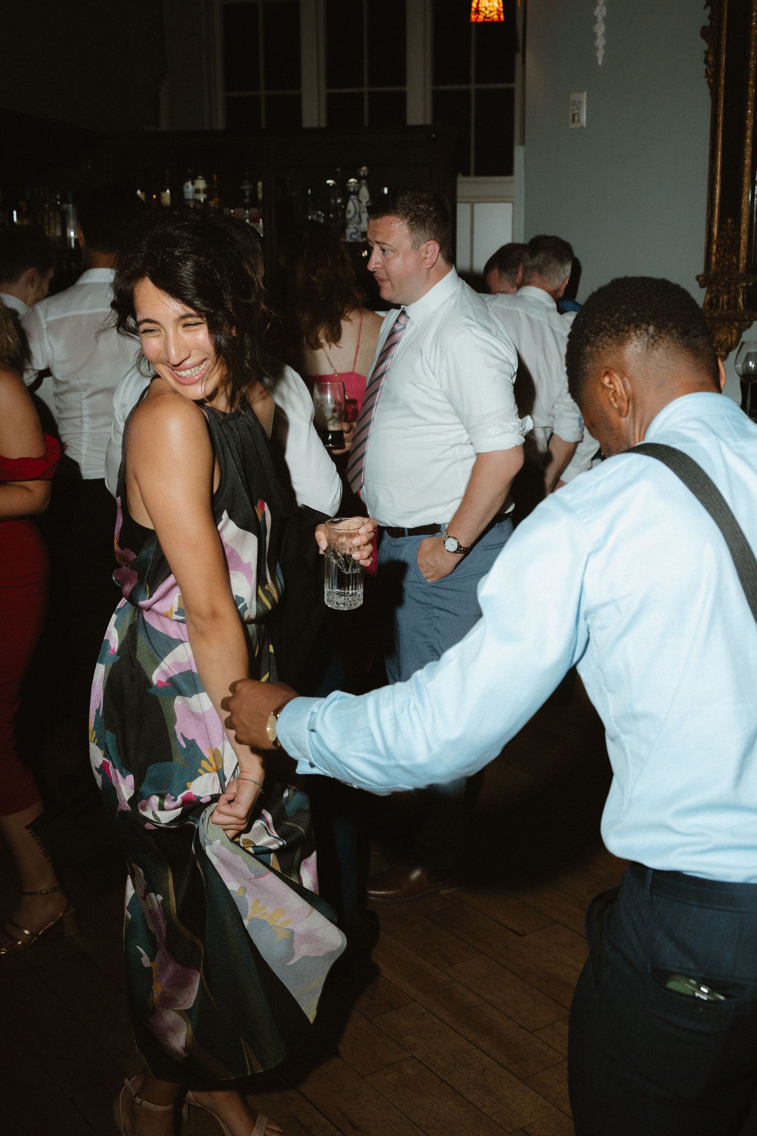 People dancing together at a dimly lit party or social gathering on a wooden dance floor.