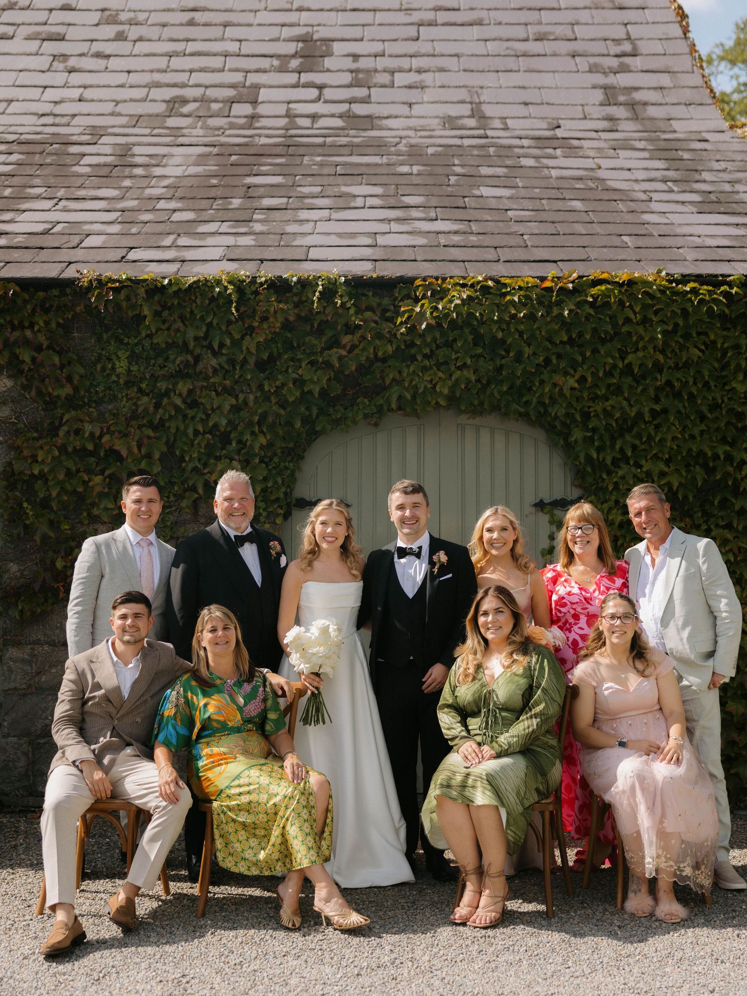 Wedding party poses in front of an ivy-covered building with slate roof.