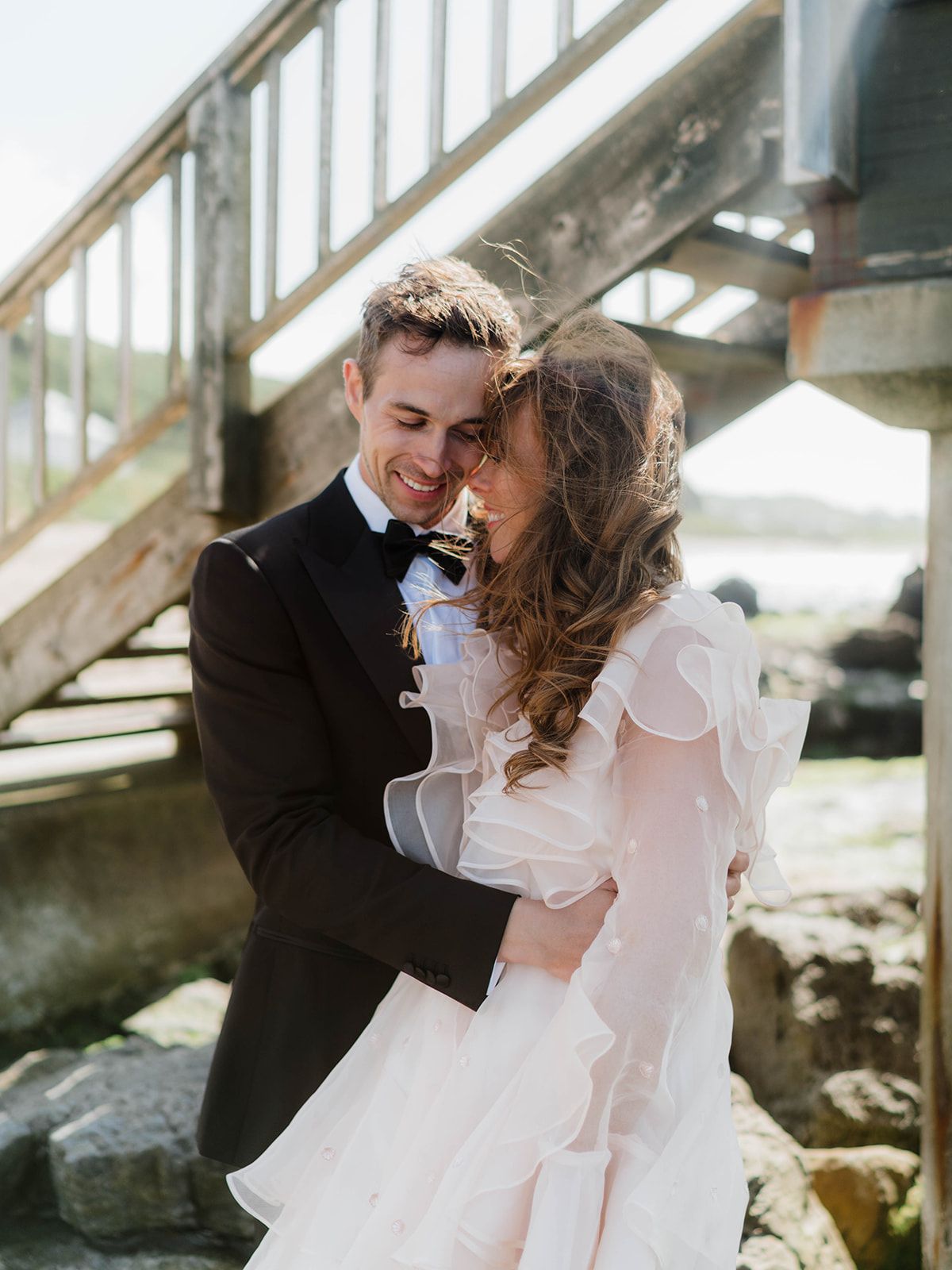 Romantic wedding couple embracing by rustic wooden stairs with the bride in a billowing white gown.